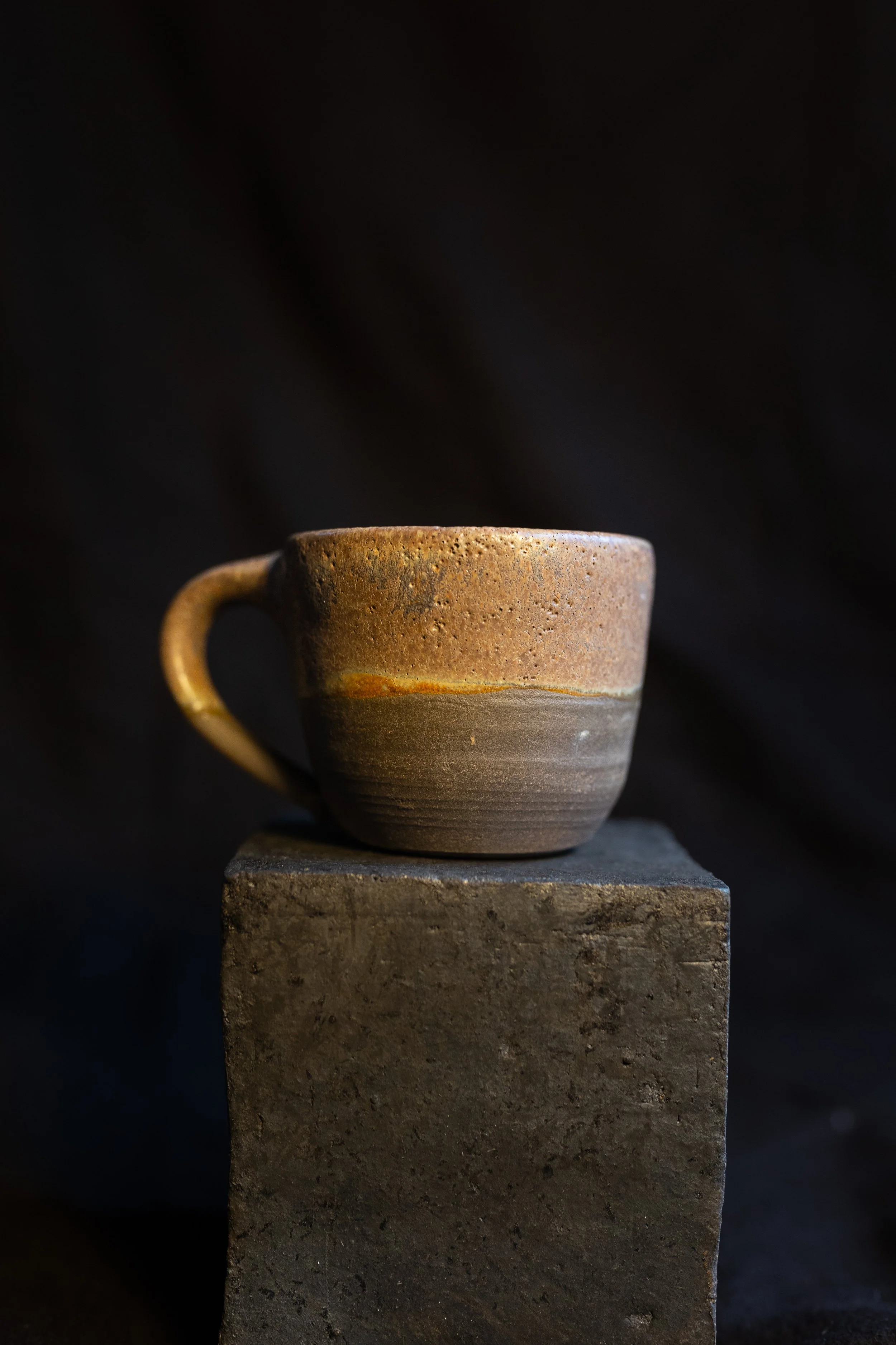 Eine handgefertigte Keramiktasse neben einem schwarzen Block auf einem dunklen Hintergrund.
