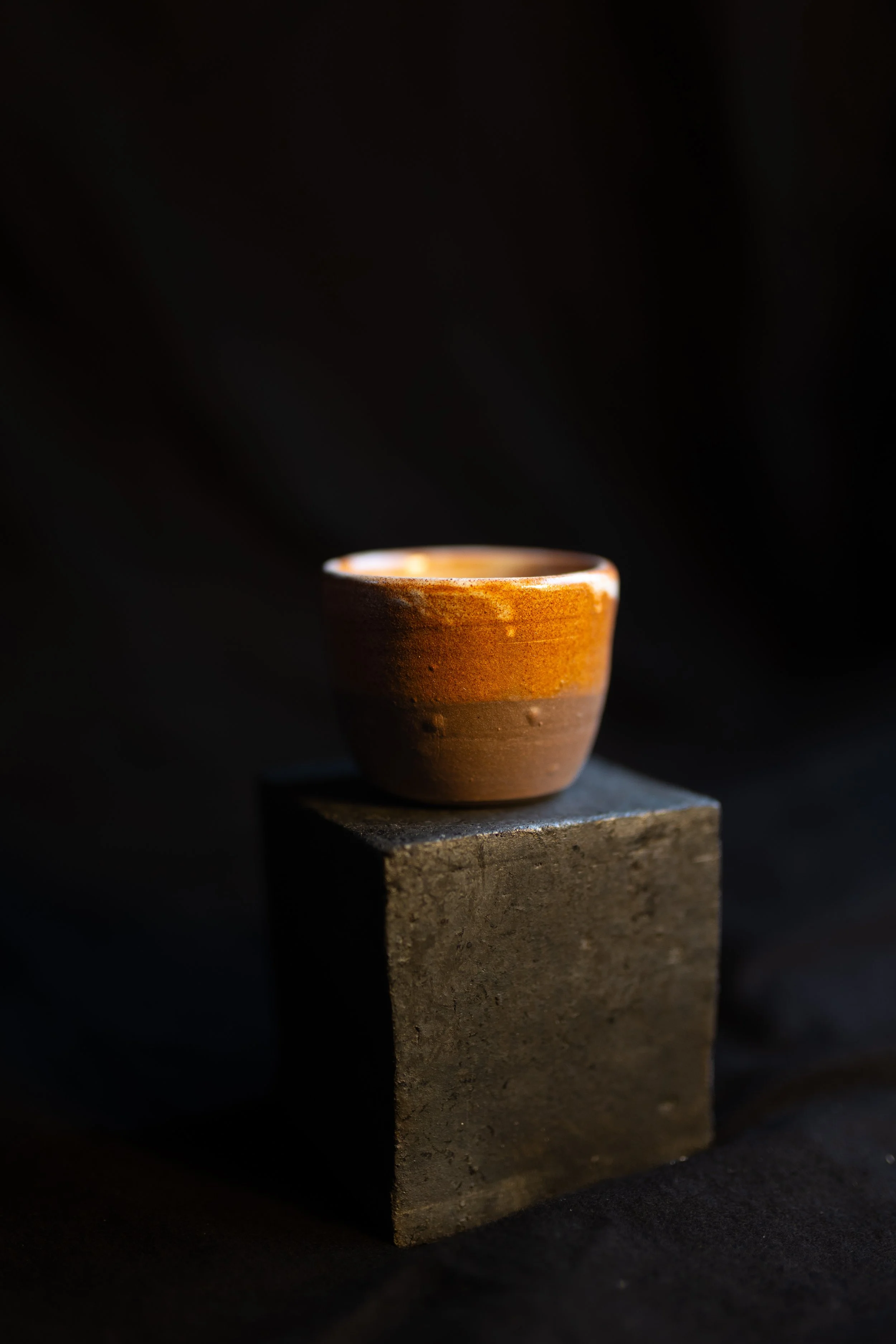 Eine kleine, mehrfarbige Keramikschale auf einem steinernen Block vor dunklem Hintergrund.