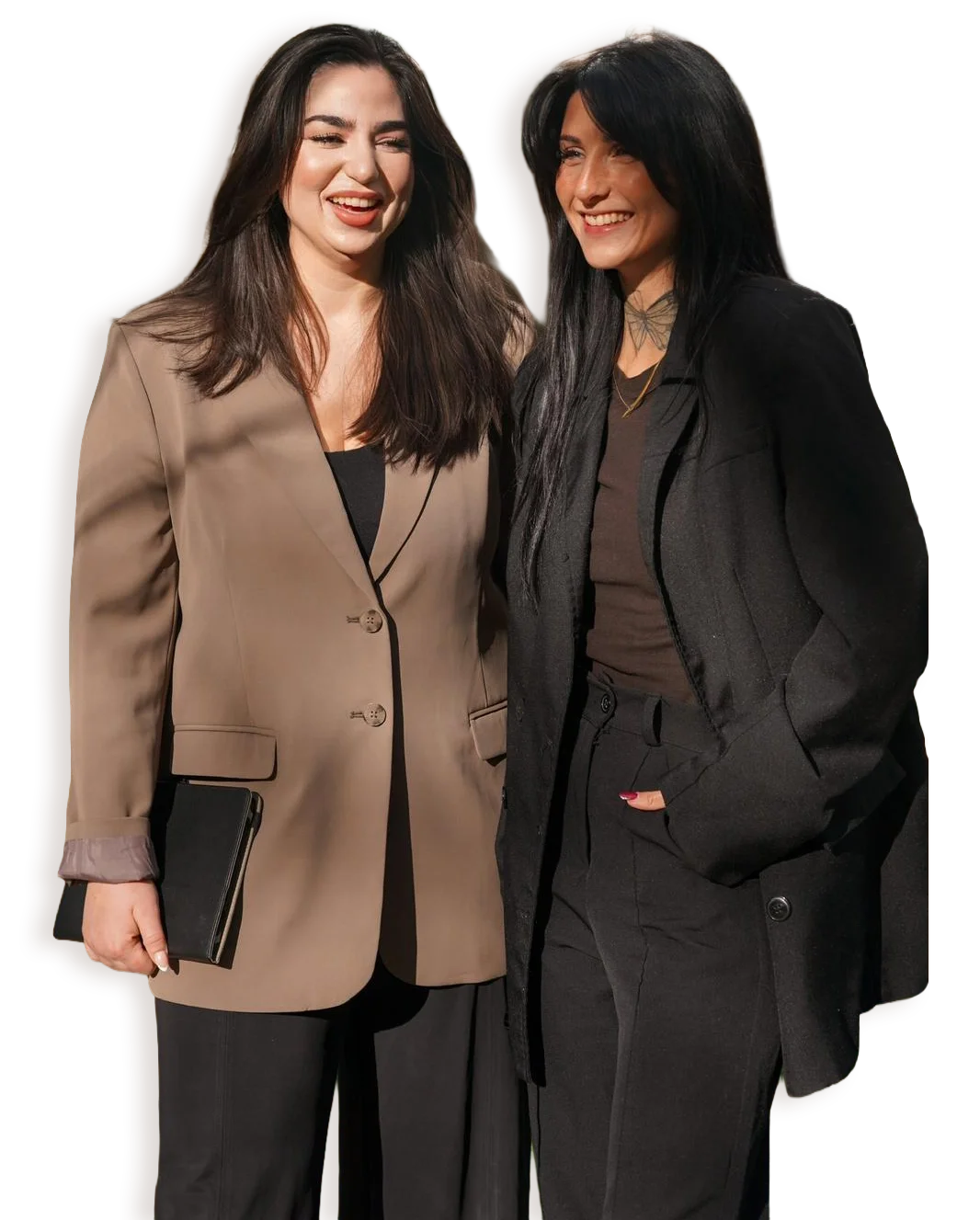 Zwei Frauen lachen und posieren zusammen in einem dunklen Hintergrund, tragen formelle Kleidung.