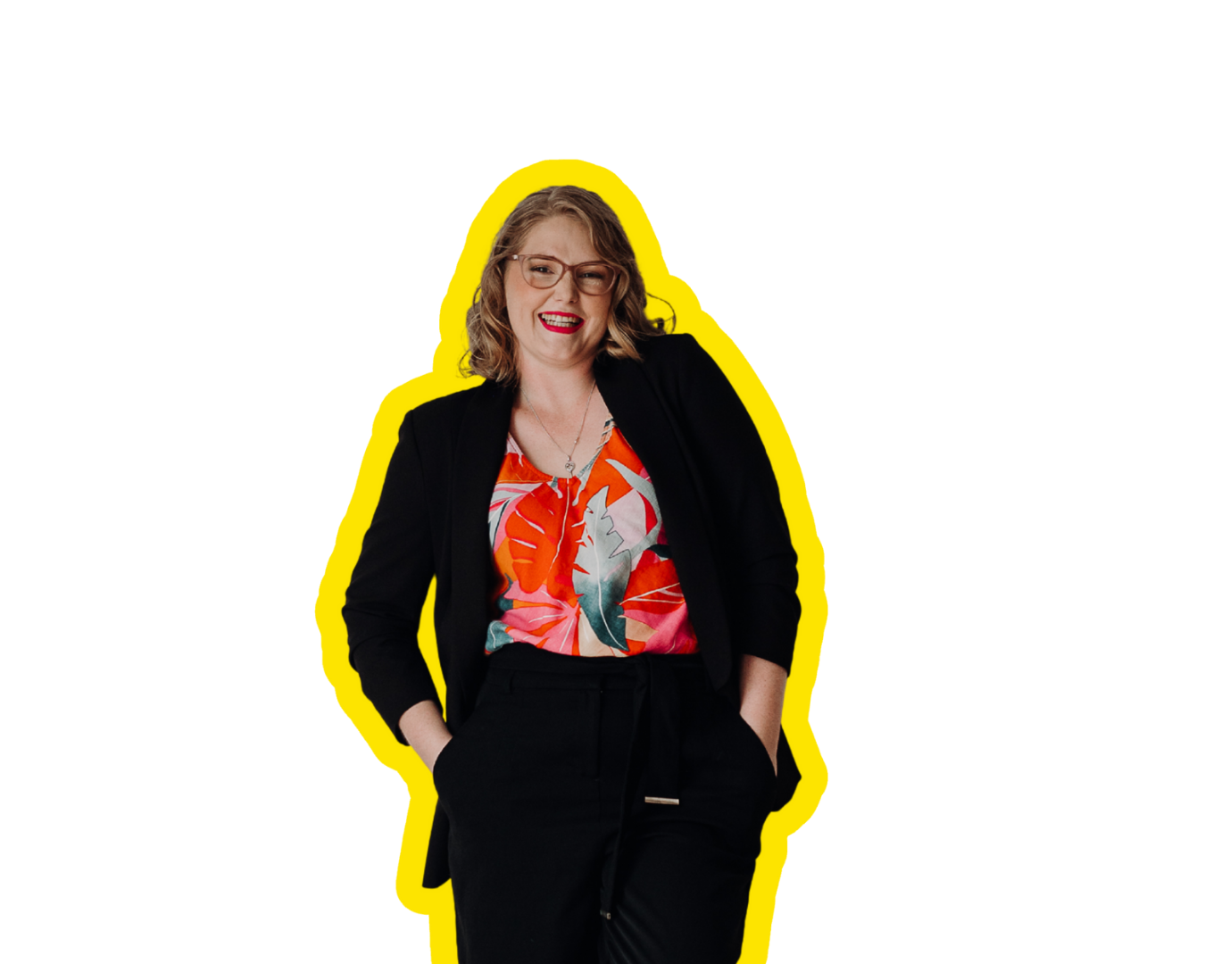 A woman with curly blonde hair, wearing glasses, a colorful tropical print blouse, and a black blazer and pants, smiling and standing with one hand in her pocket.