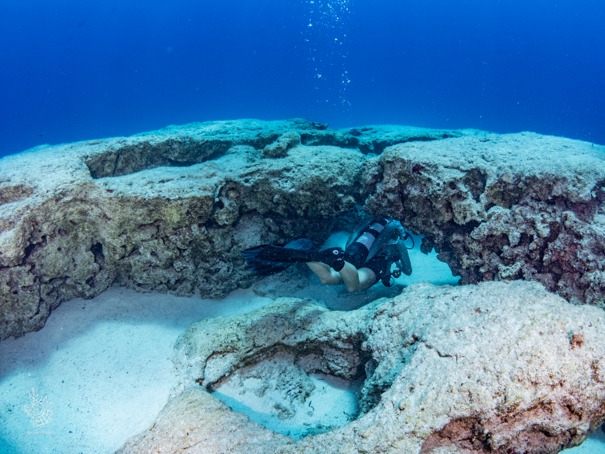 A scuba diver exploring a rocky underwater formation with a sandy bottom.