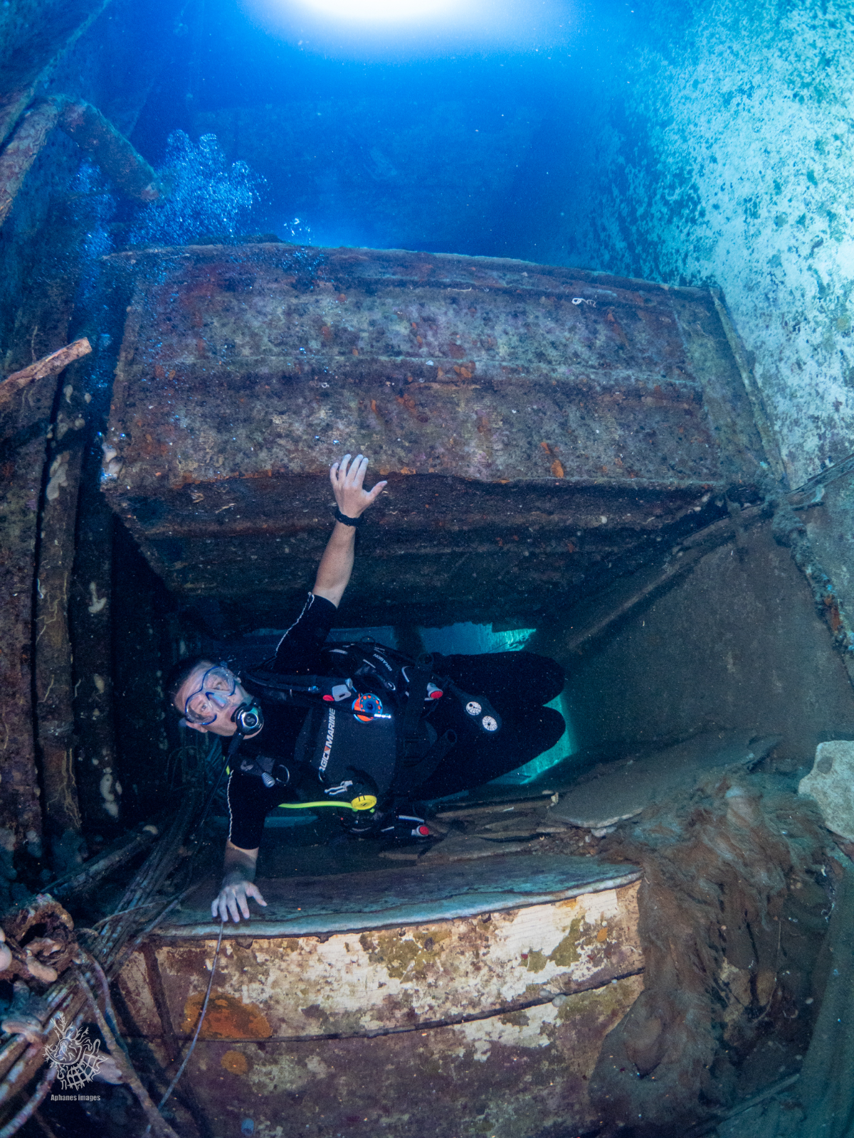 Scuba diver exploring a sunken shipwreck, holding onto a large rusted metal section of the wreck underwater.