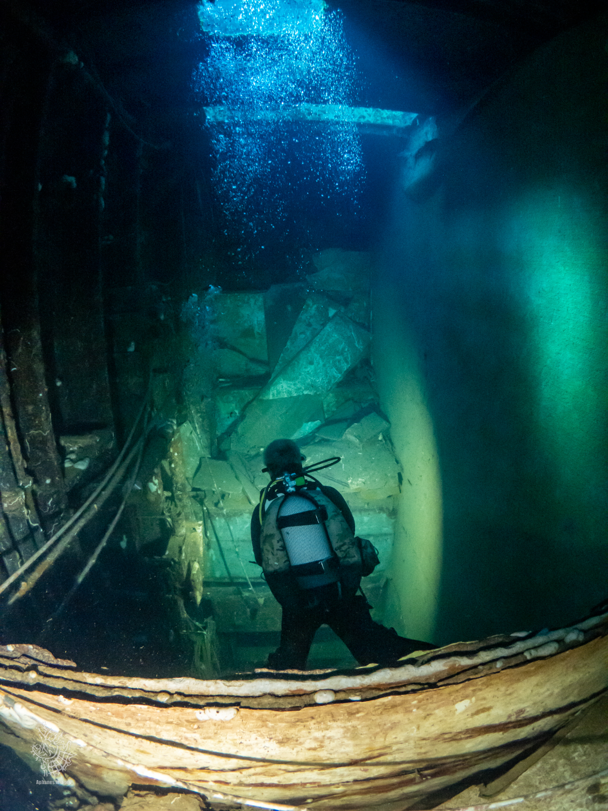A diver in scuba gear exploring an underwater wreck with debris and bubbles.