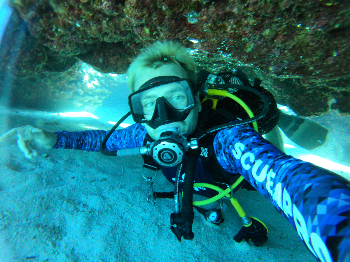 Scuba diver exploring underwater rocks and sandy seabed.