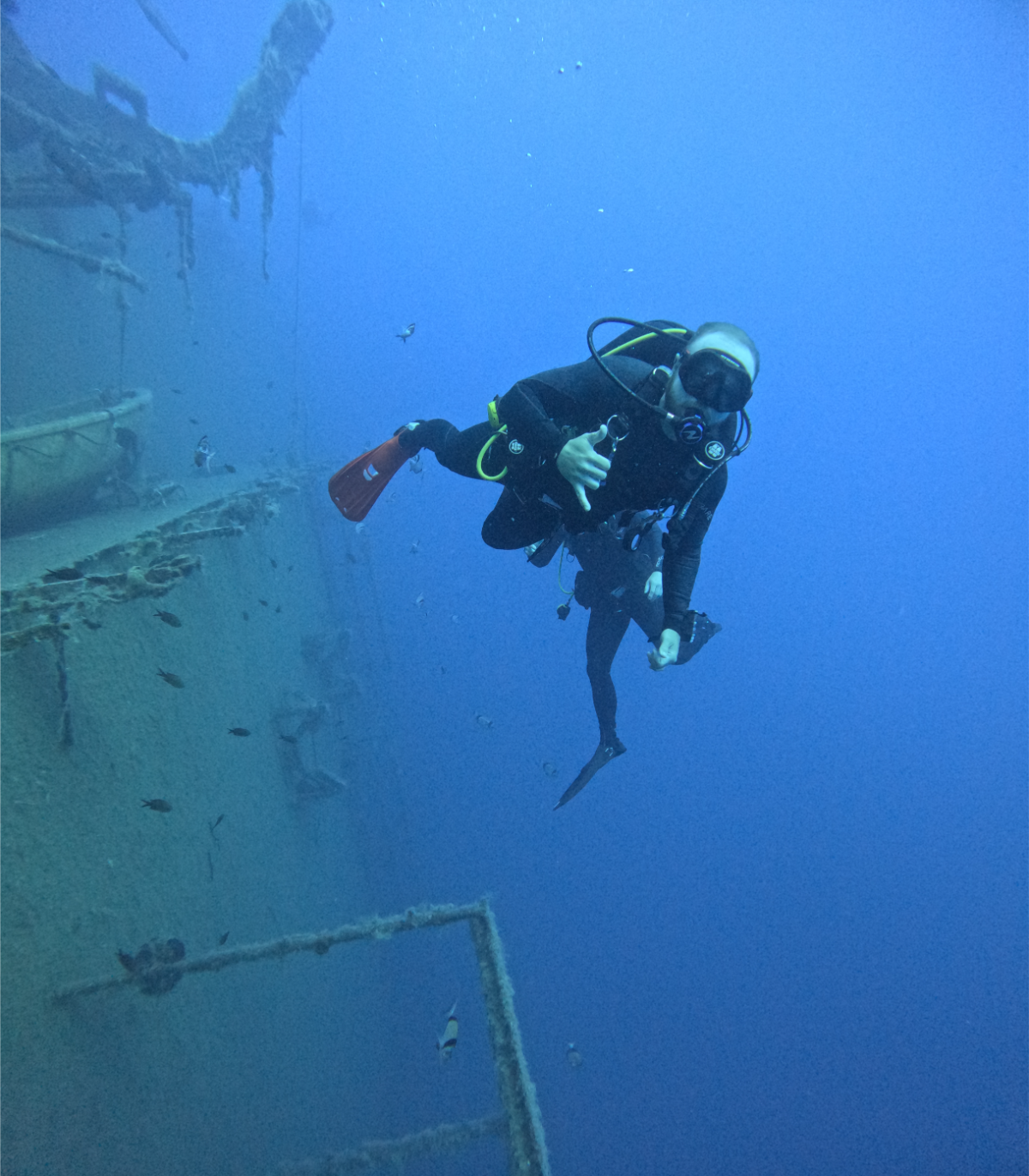 A scuba diver underwater near a shipwreckwreck, showing the diver giving a thumbs-up gesture.