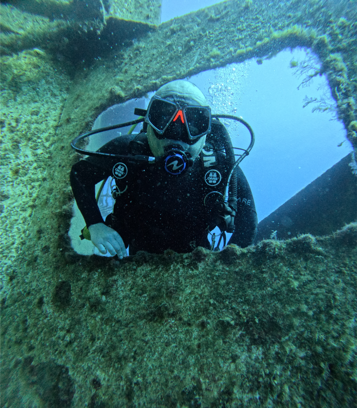 A scuba diver in full gear exploring underwater near a sunken structure or wreck.
