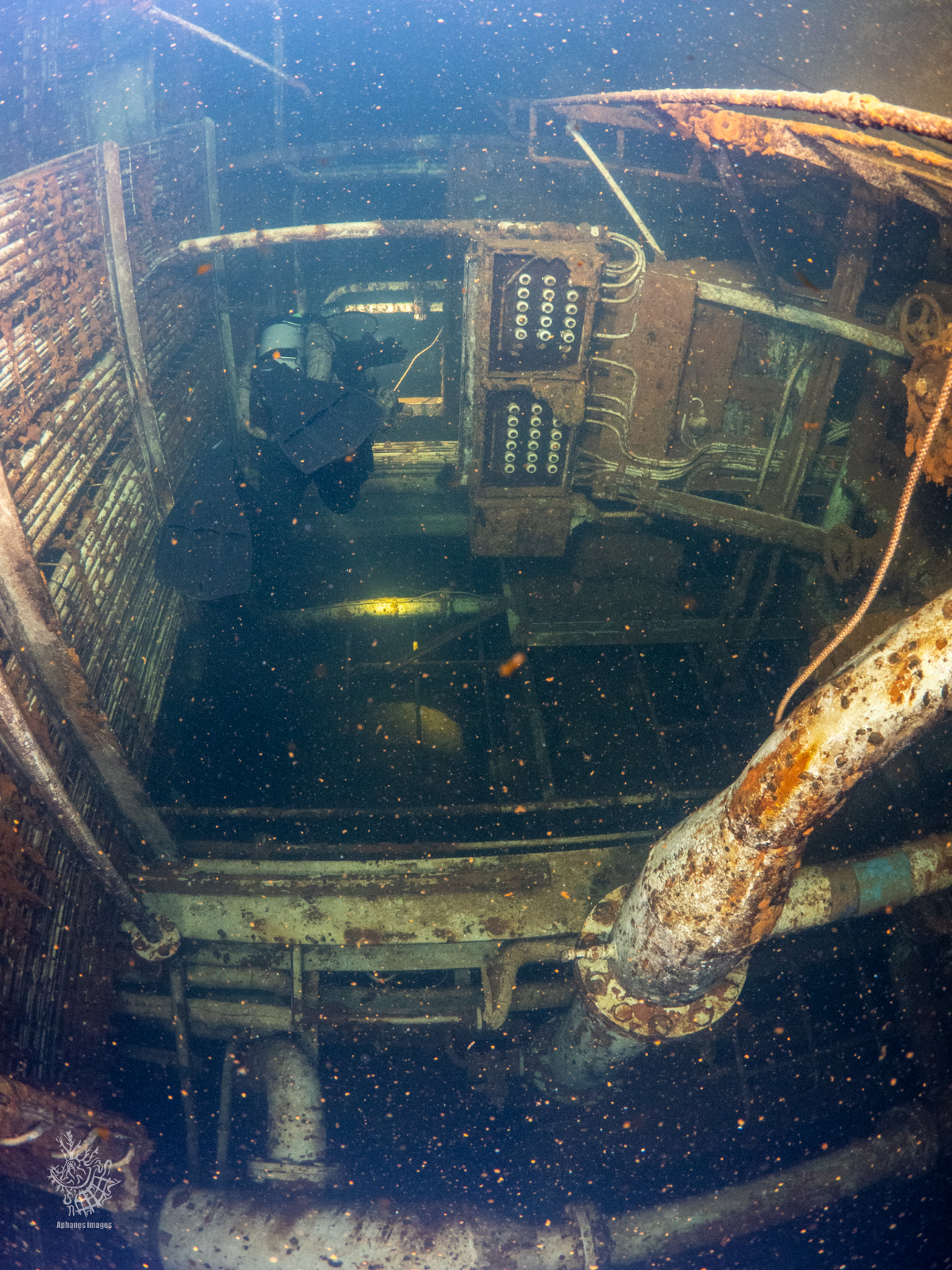 Underwater photograph of a sunken, rusted submarine's control room with a person inspecting the equipment.