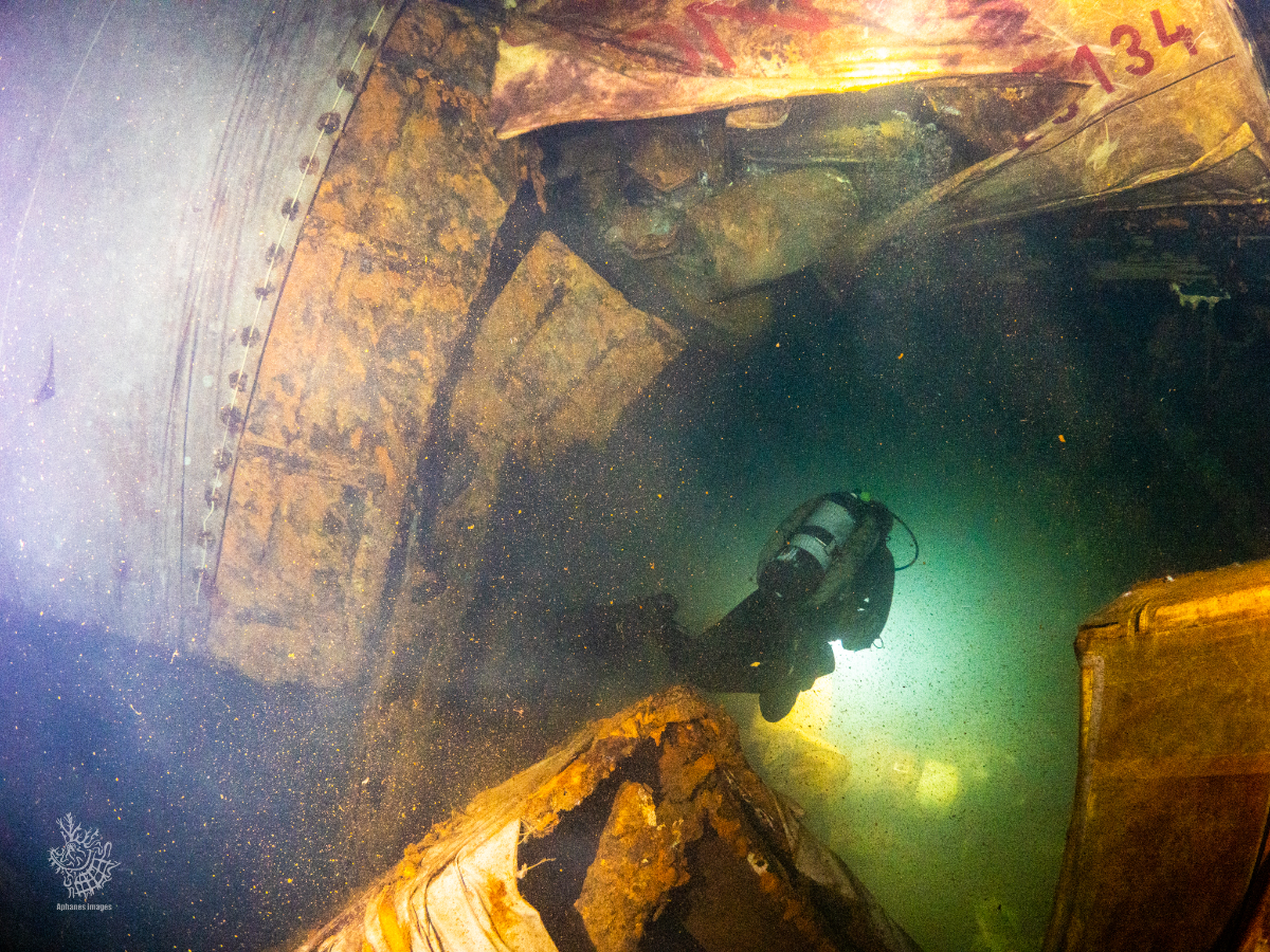 A diver exploring a sunken shipwreck underwater, surrounded by rusted metal and debris.