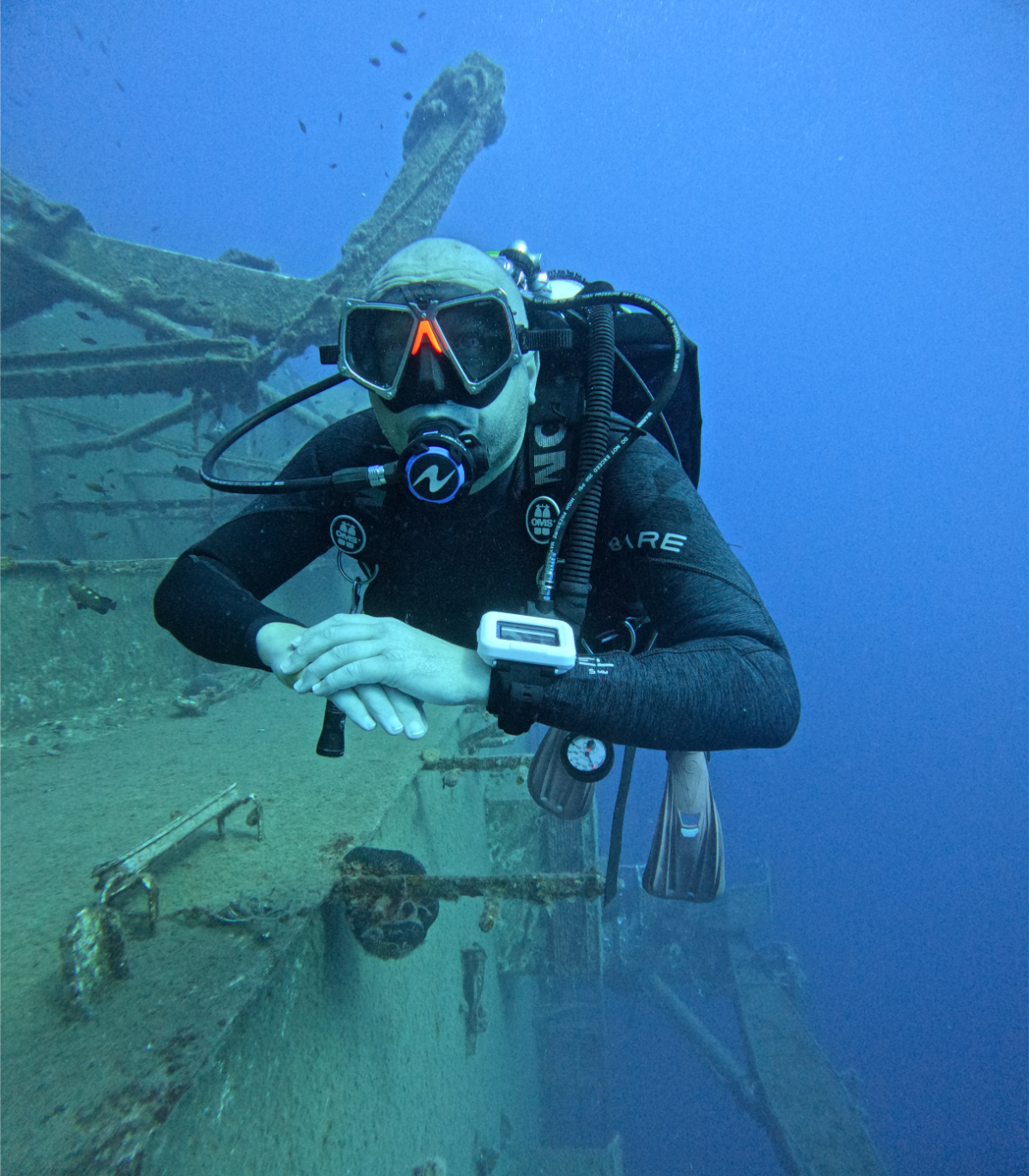 Scuba diver underwater examining wreckage with debris and coral growth.