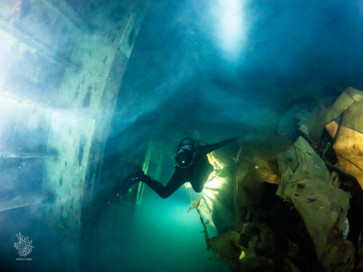 A scuba diver exploring an underwater shipwreck with submerged debris and rocks.