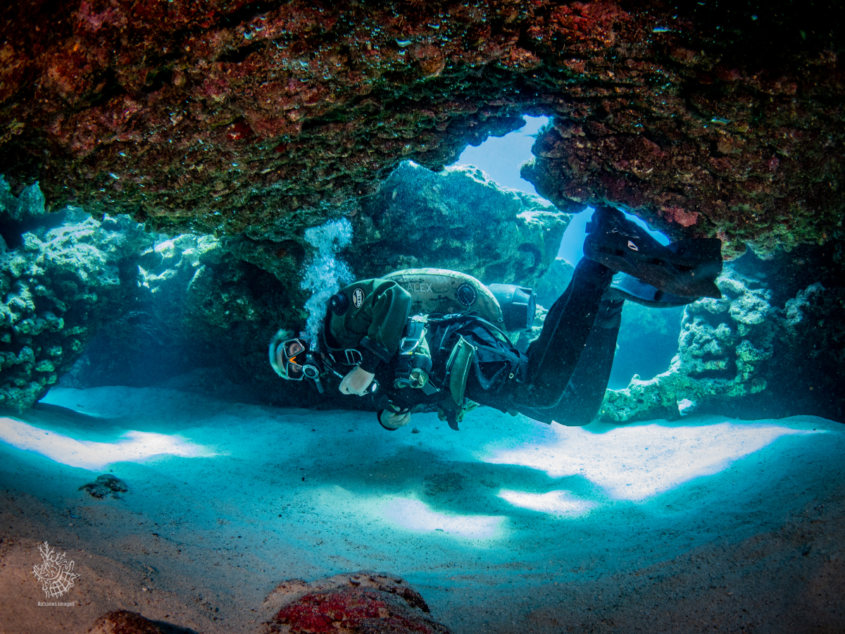 An underwater scene with a scuba diver exploring a coral cave.