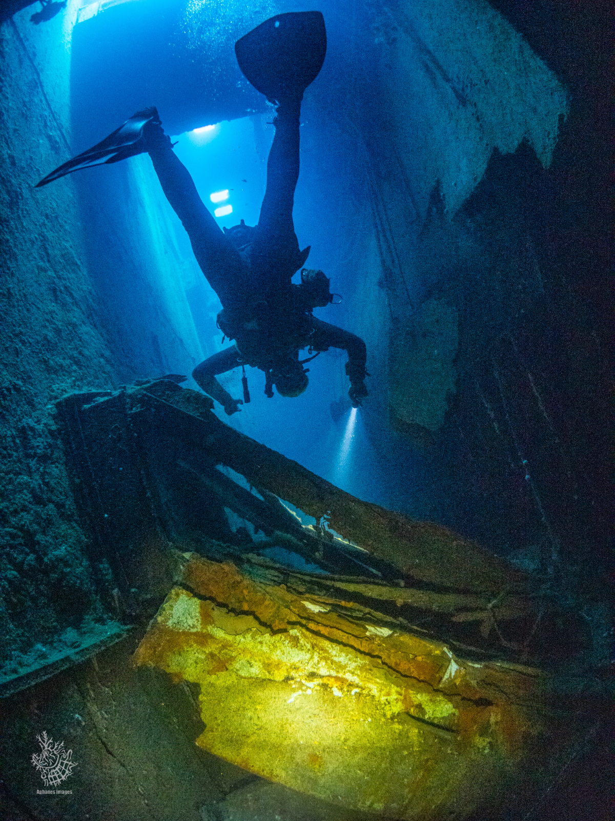 A scuba diver exploring the underwater interior of a sunken shipwreck with a flashlight.