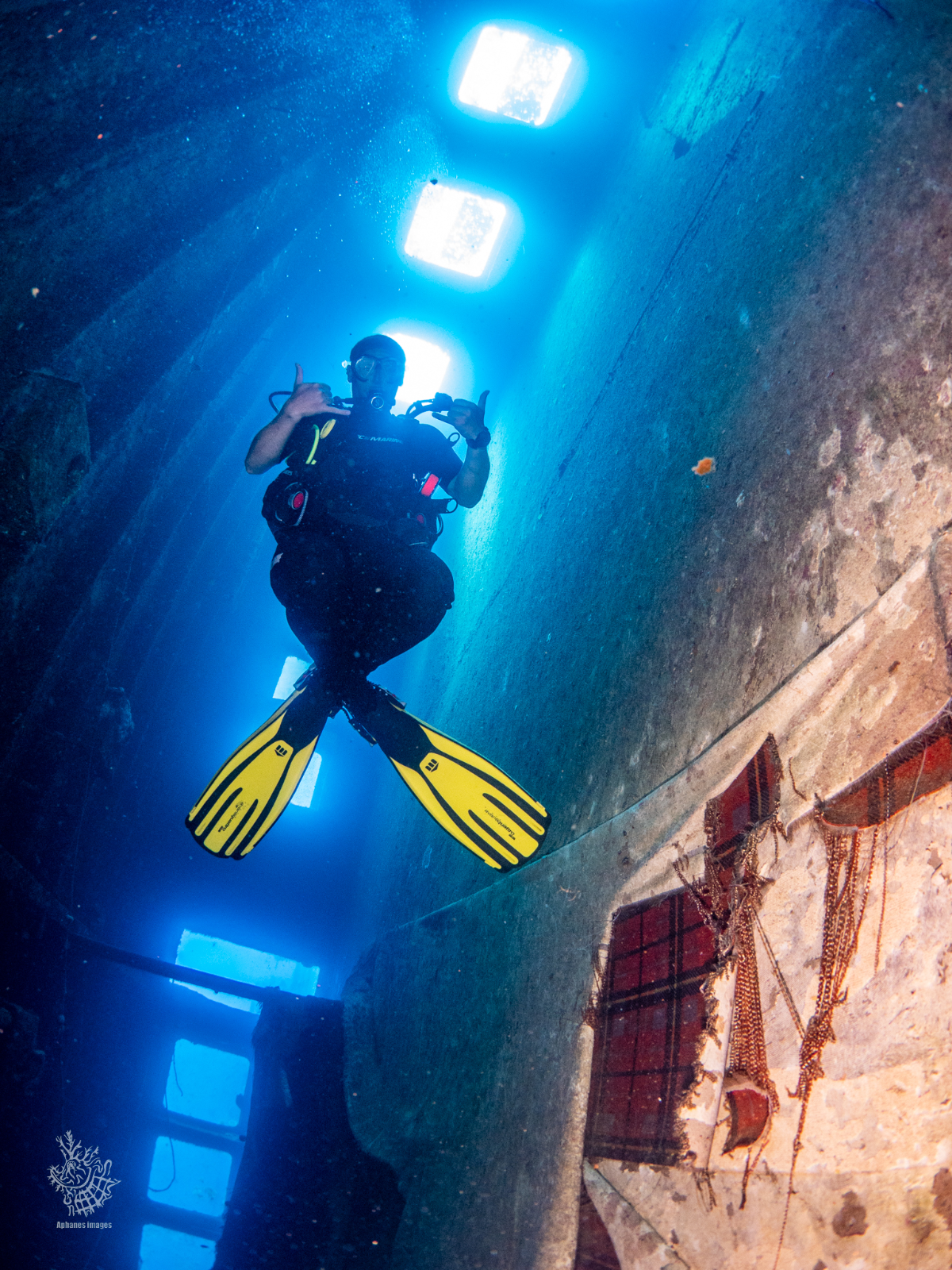 A scuba diver with yellow fins underwater inside a sunken structure with rectangular openings