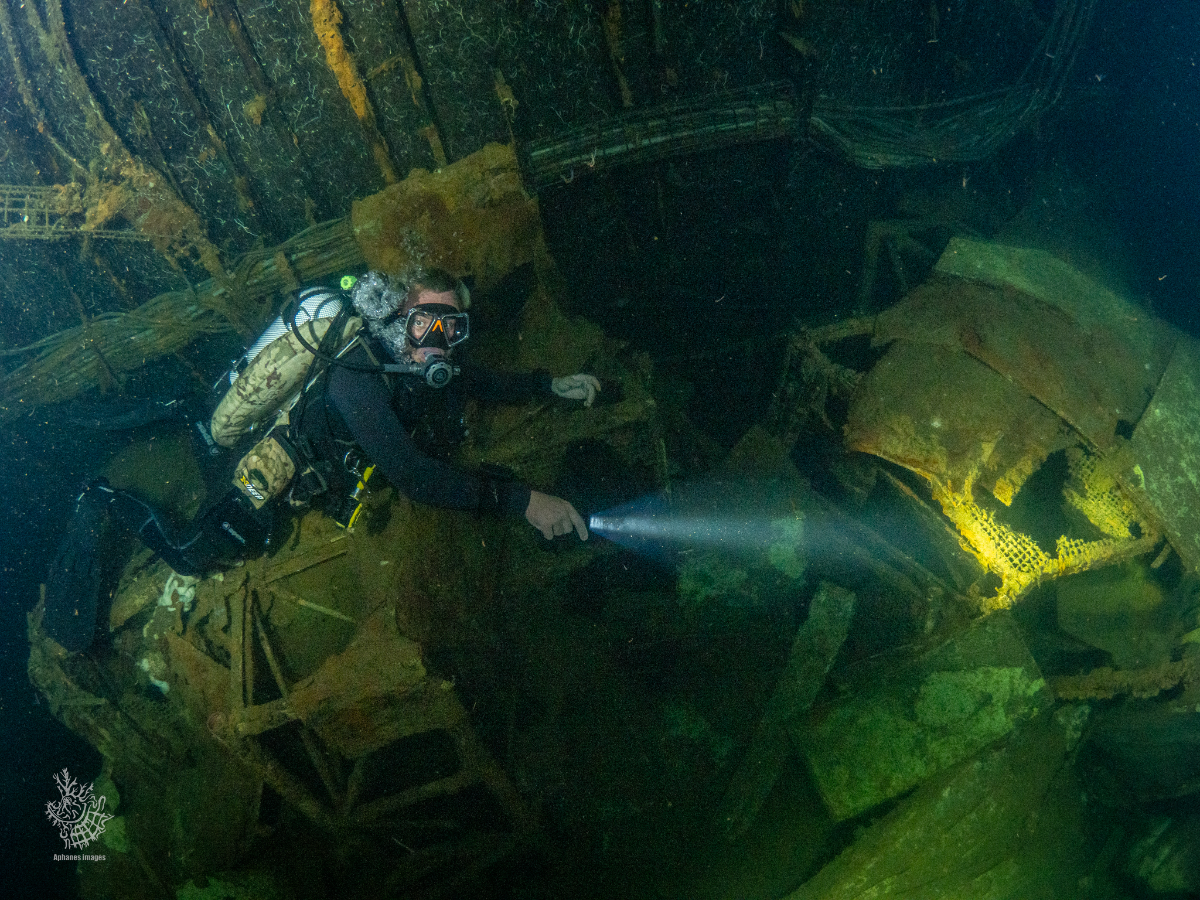 A scuba diver explores the interior of the Zenobia in Larnaca Cyprus, equipped with underwater gear, flashlight, and diving suit.