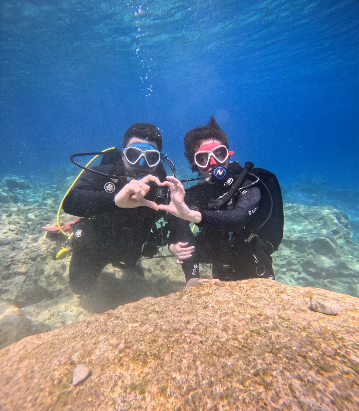 Two scuba divers underwater making a heart shape with their hands.