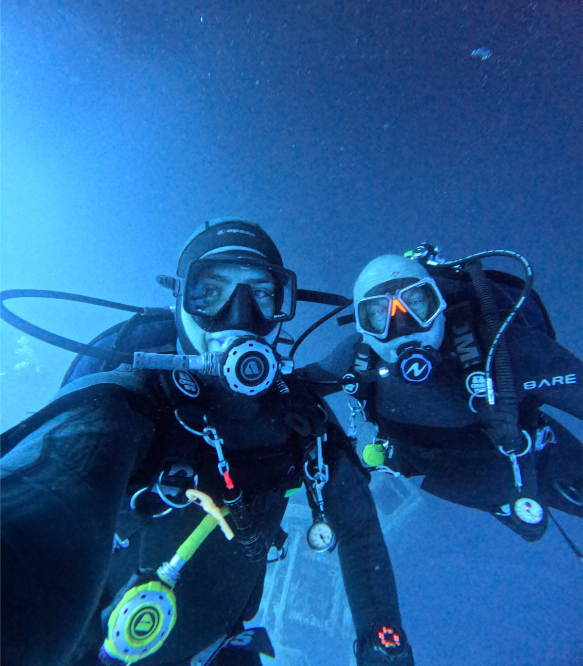 Two scuba divers underwater taking a selfie, wearing masks and tanks.