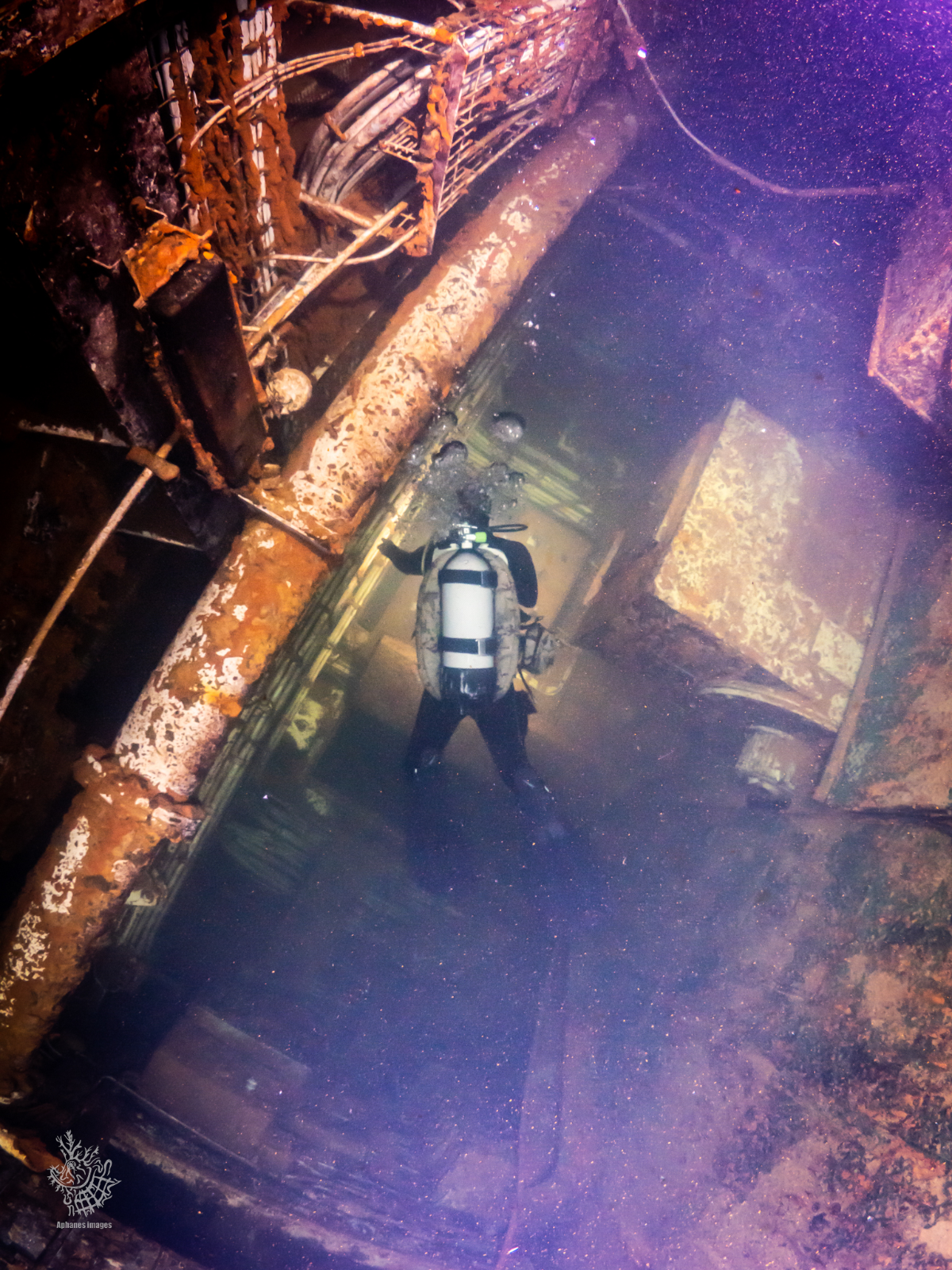 Scuba diver exploring the interior of a sunken shipwreck with rusted metal structures and debris.