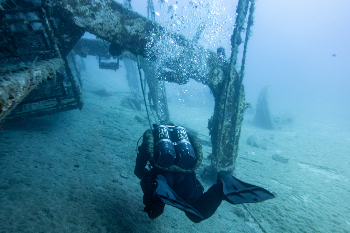 A diver exploring a sunken, abandoned shipwreck underwater.