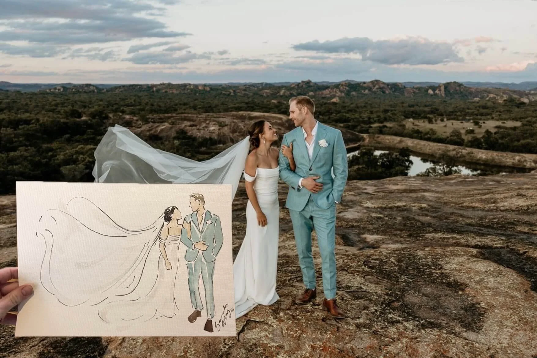 A couple dressed in wedding attire standing on a rocky landscape with a river and hilly terrain in the background during sunset. The woman wears a white dress with a long veil, and the man wears a light blue suit.