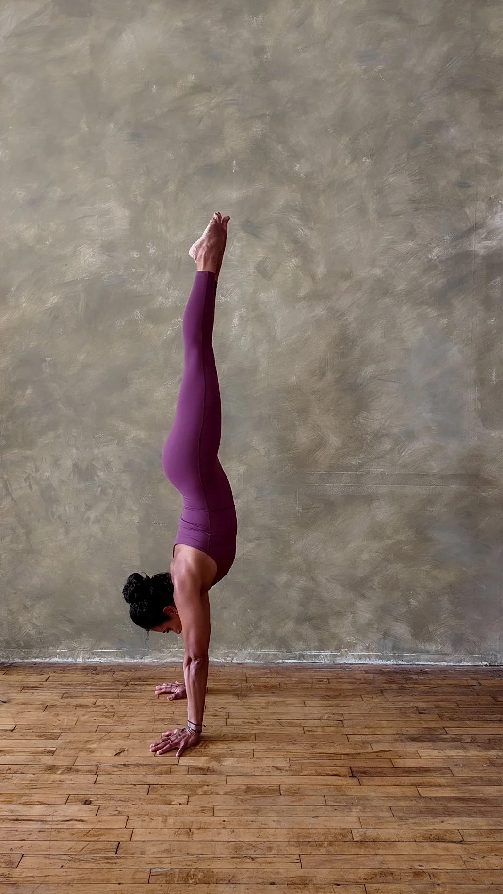 A woman practicing yoga indoors, performing a handstand with her body straight and her legs extended upward.