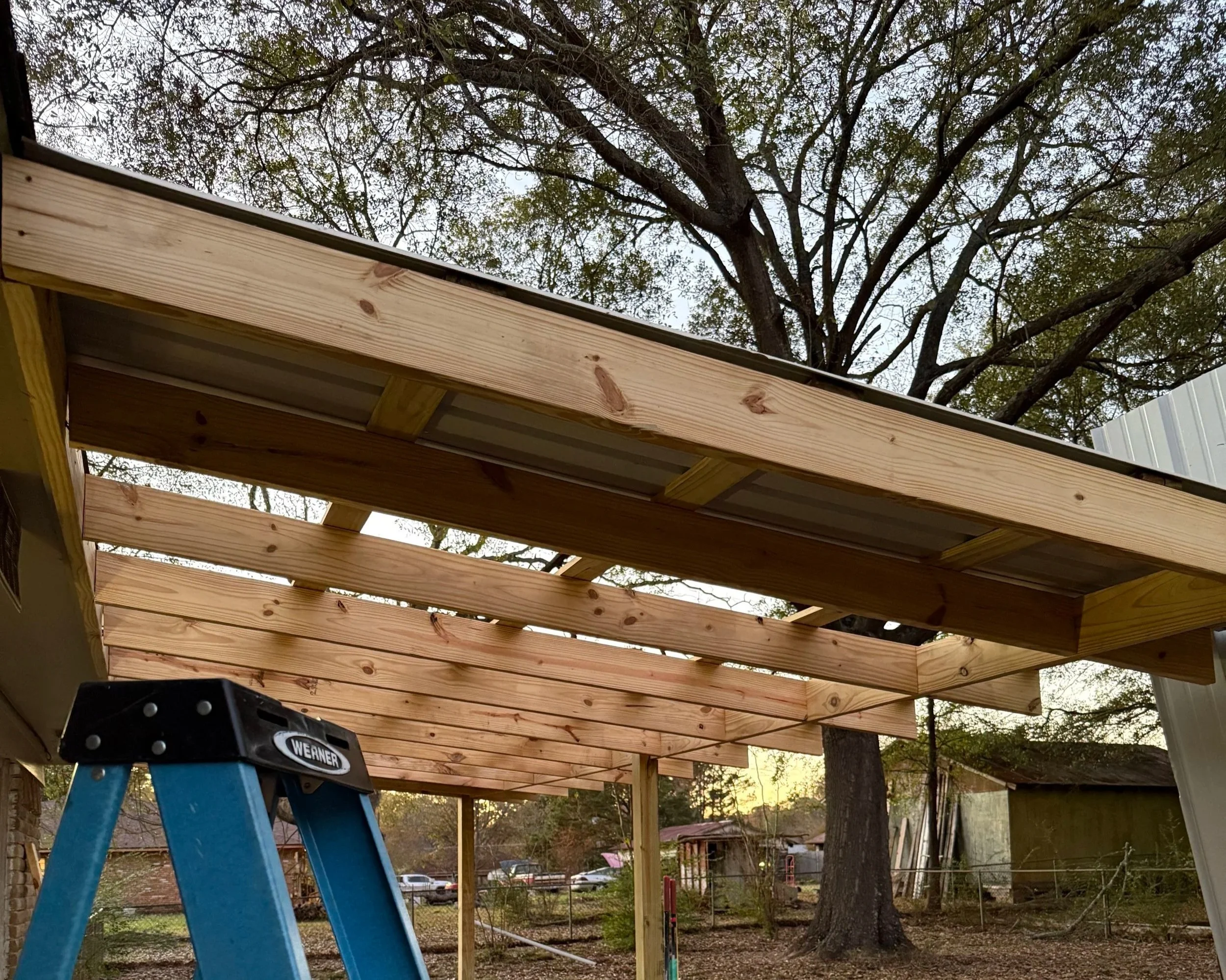 Wooden porch or deck under construction with a ladder and trees in the background.
