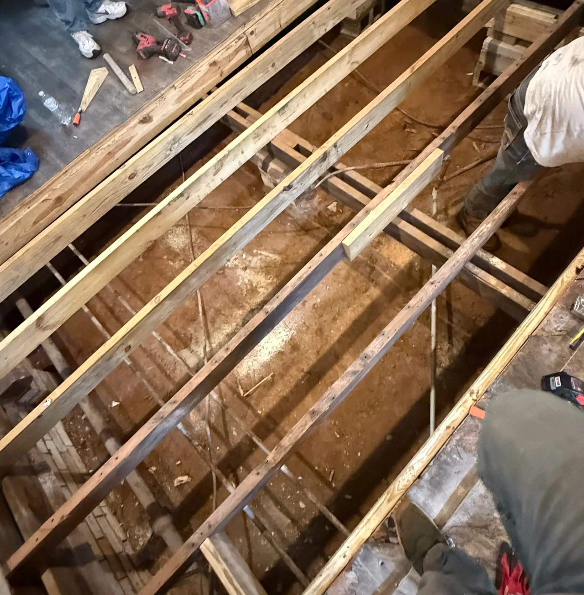 Construction site showing wooden framing for a floor or wall, with tools and equipment nearby.