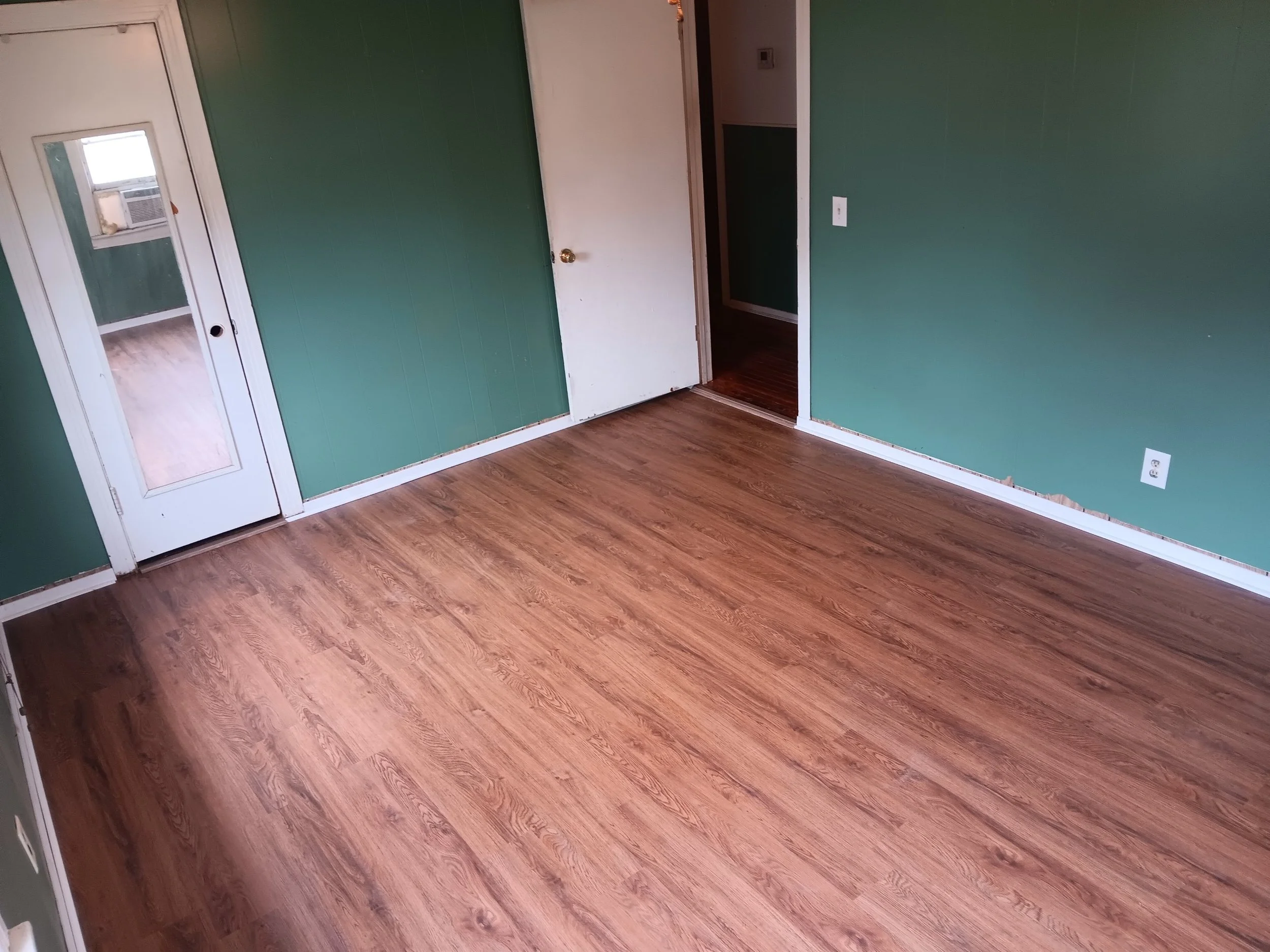 Empty room with green walls, hardwood floor, a white door, and a glass-paneled door leading outside.
