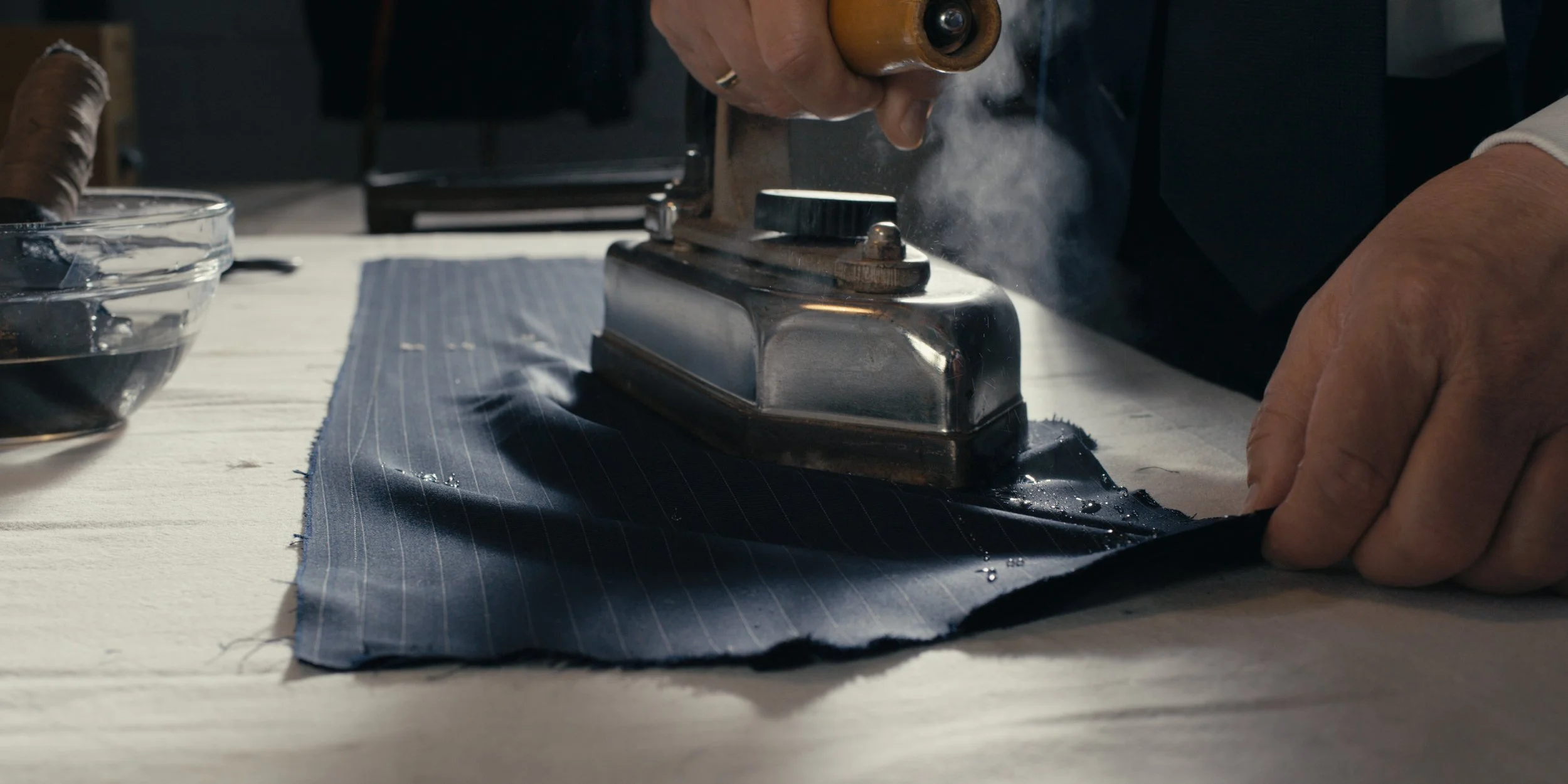 Eine Person bügelt einen Stoff mit einem Bügeleisen auf einem Tisch.