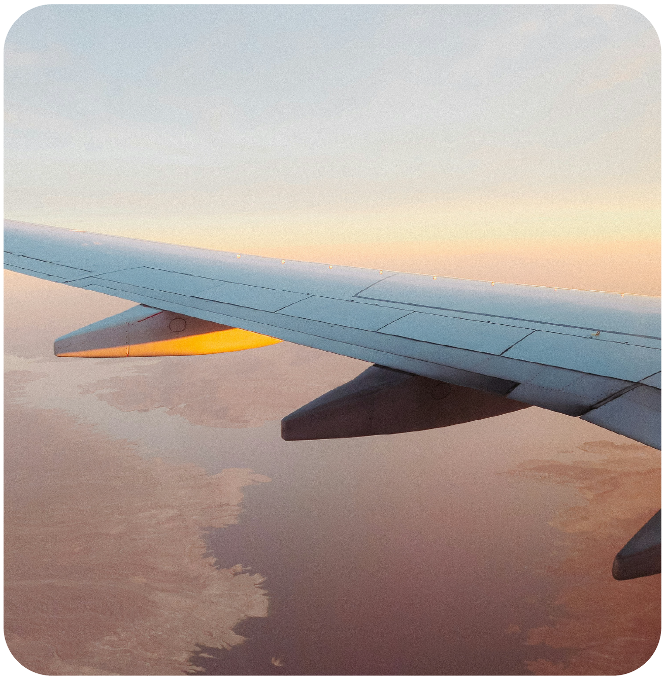 Airplane wing flying above the clouds during sunset.