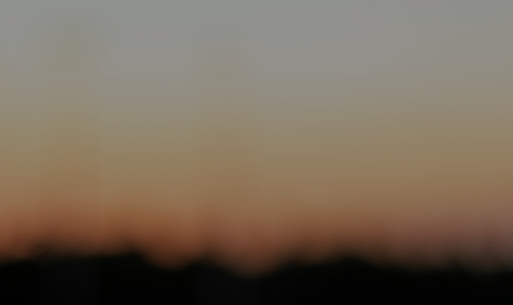 blurred sunset scene with a gradient sky transitioning from orange to gray, over silhouettes of mountains or hills.