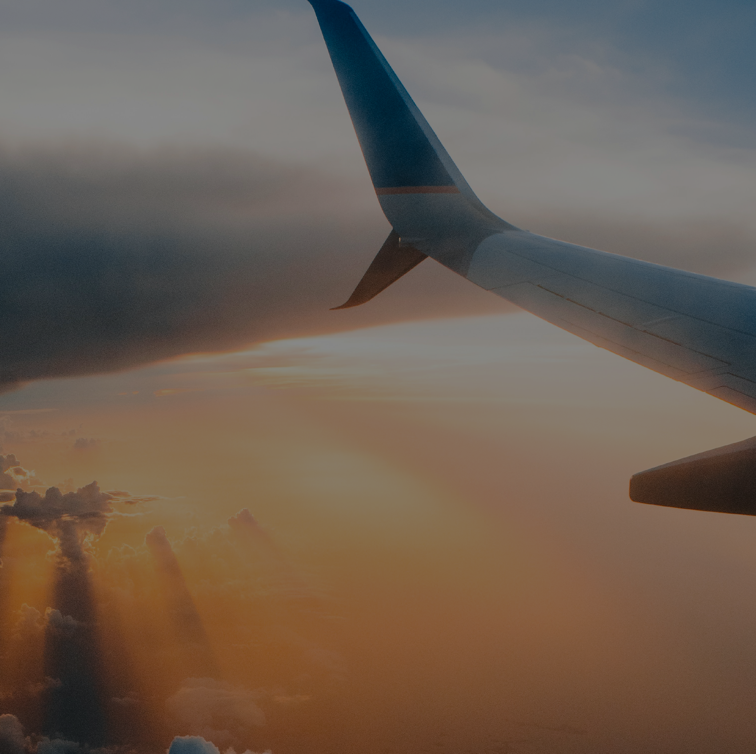 View of an airplane wing at sunset, with clouds and sunlight in the background.