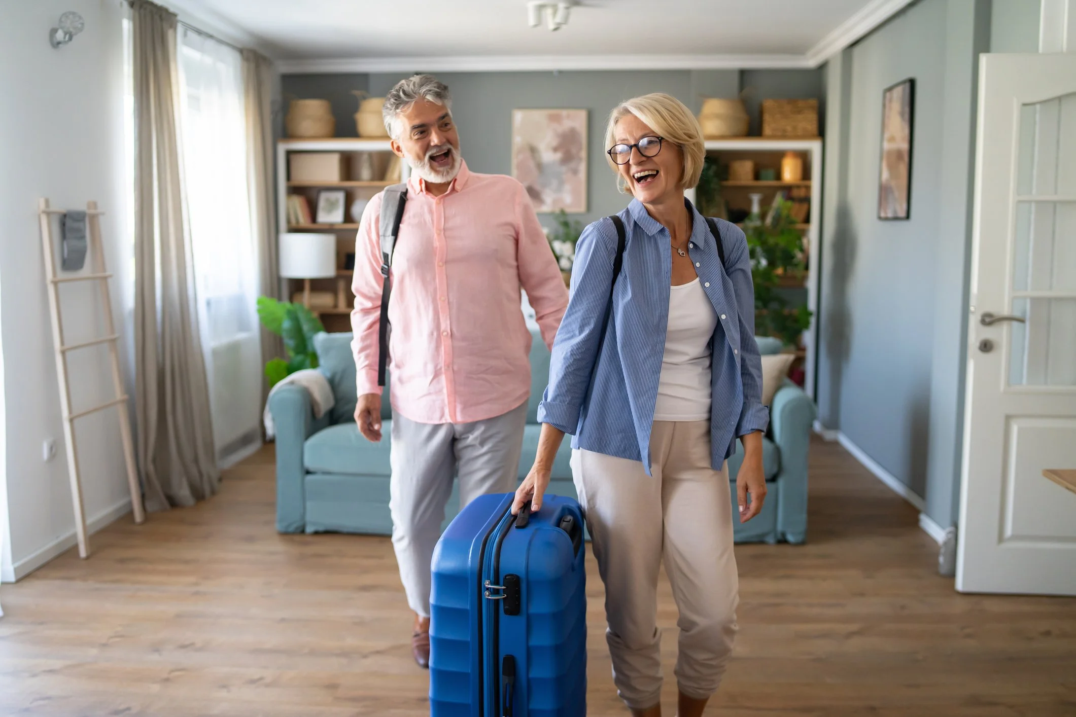 A senior couple with bags walking into a home, smiling and enjoying their visit.