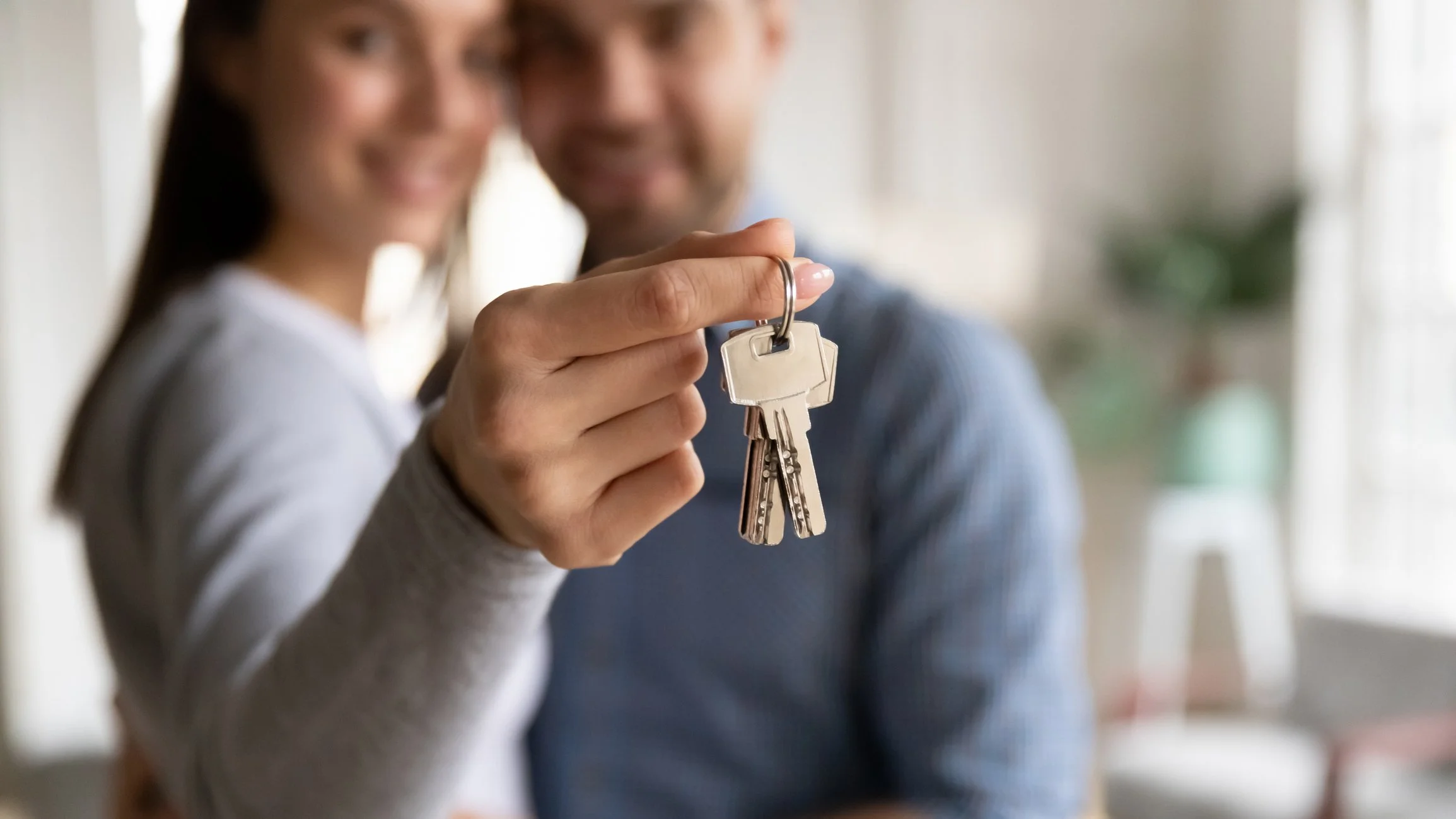 A woman and a man are smiling, with the woman holding out a keychain with keys towards the camera.
