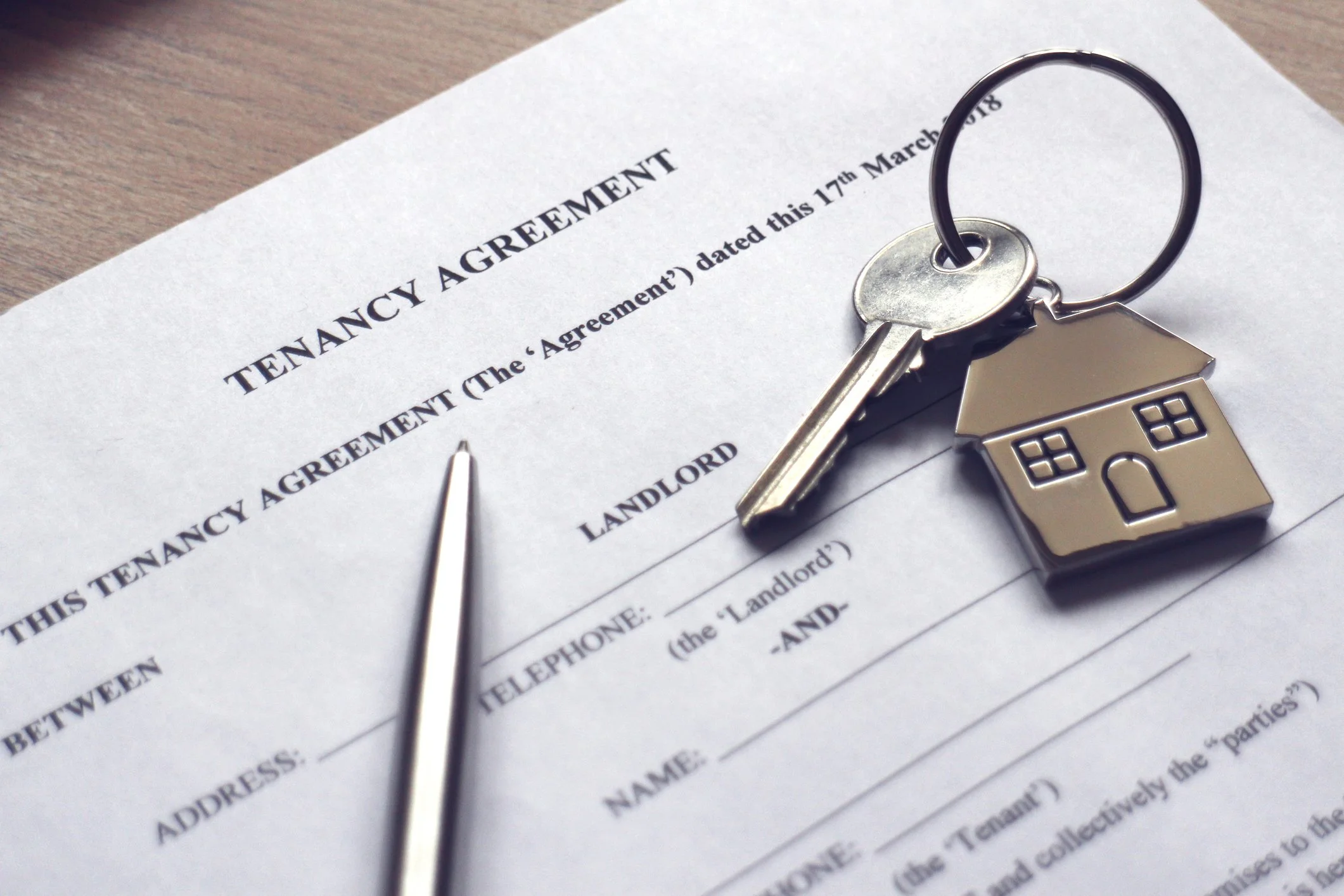 A tenancy agreement form with a silver key and house-shaped keychain on top of it.