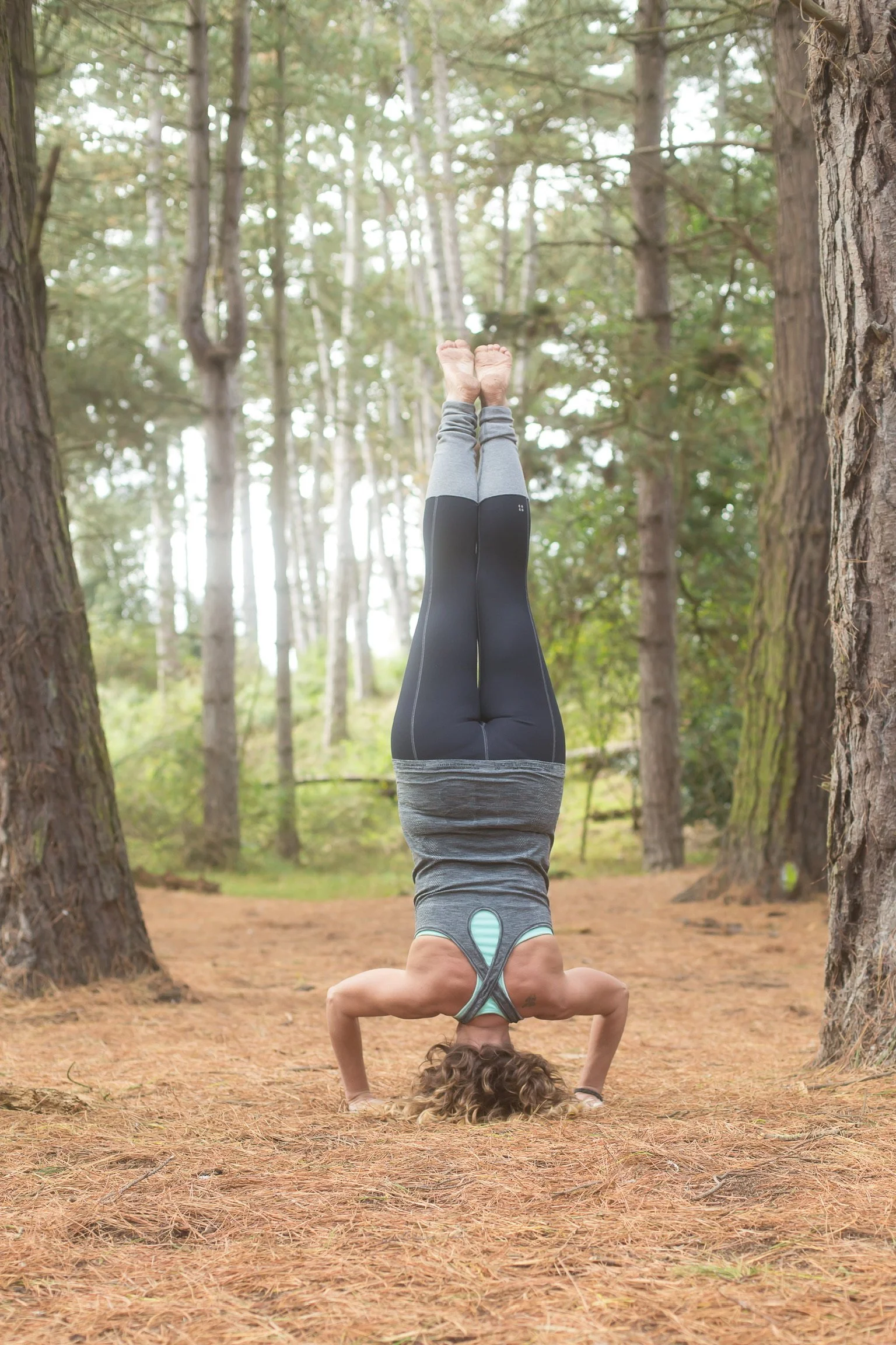 Jax Heffer-Cooke performing a headstand yoga pose in a forest, surrounded by trees and pine needles on the ground.