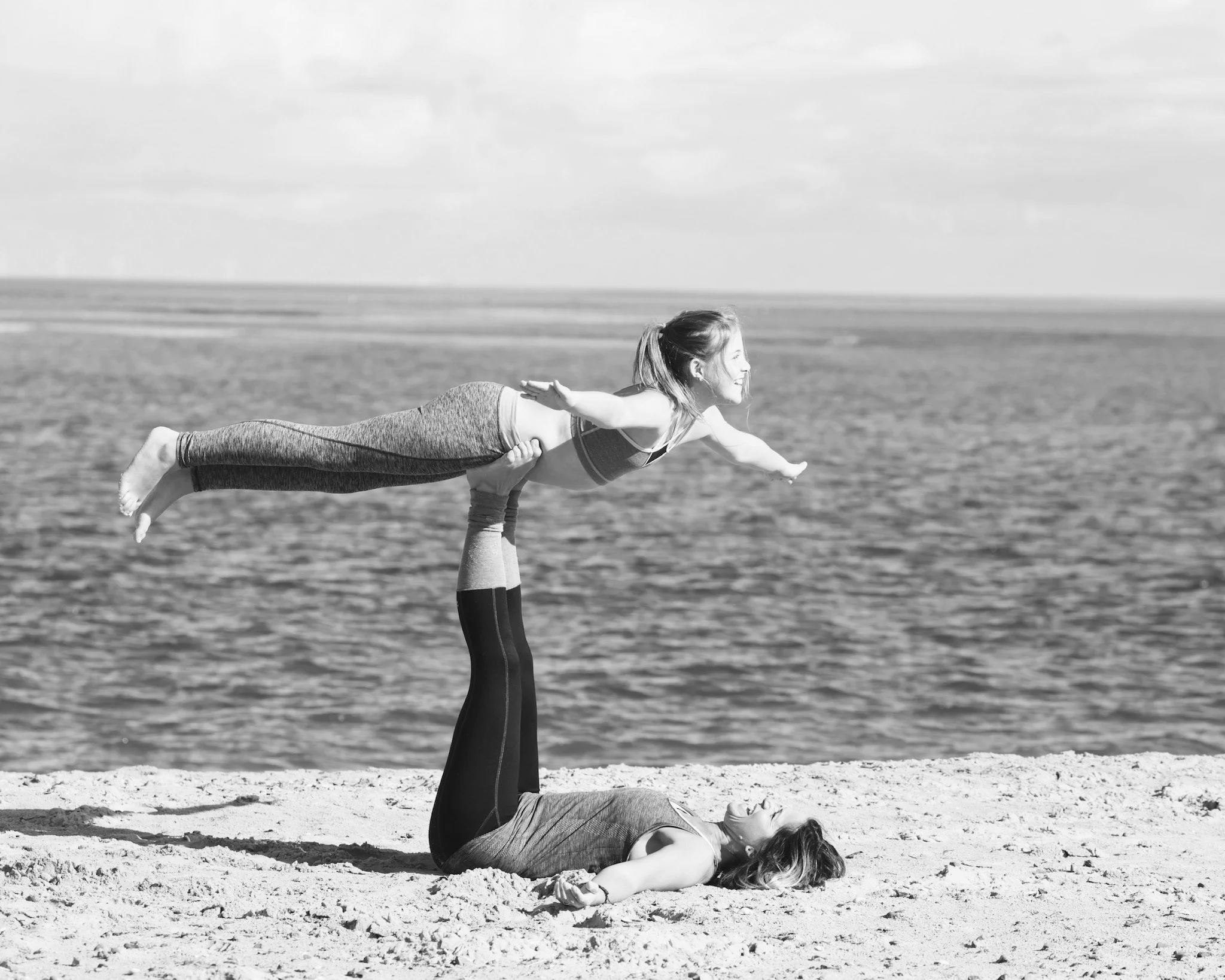 Two women practicing Bird Pose yoga on the beach