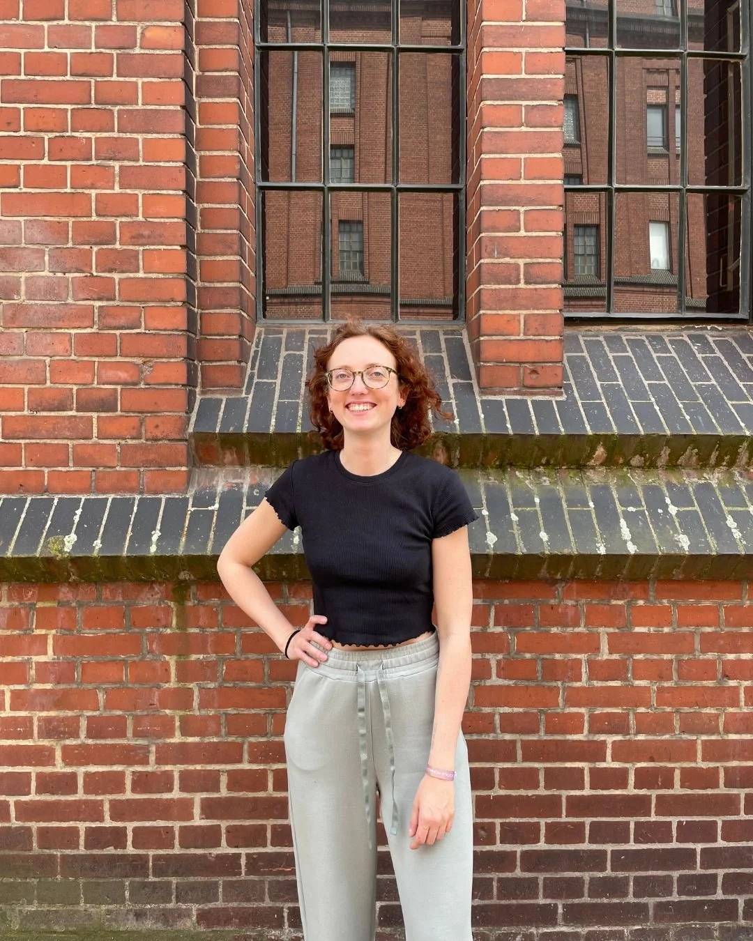Mira Kullmann steht vor einer roten Backsteinwand mit großen Fenstern.