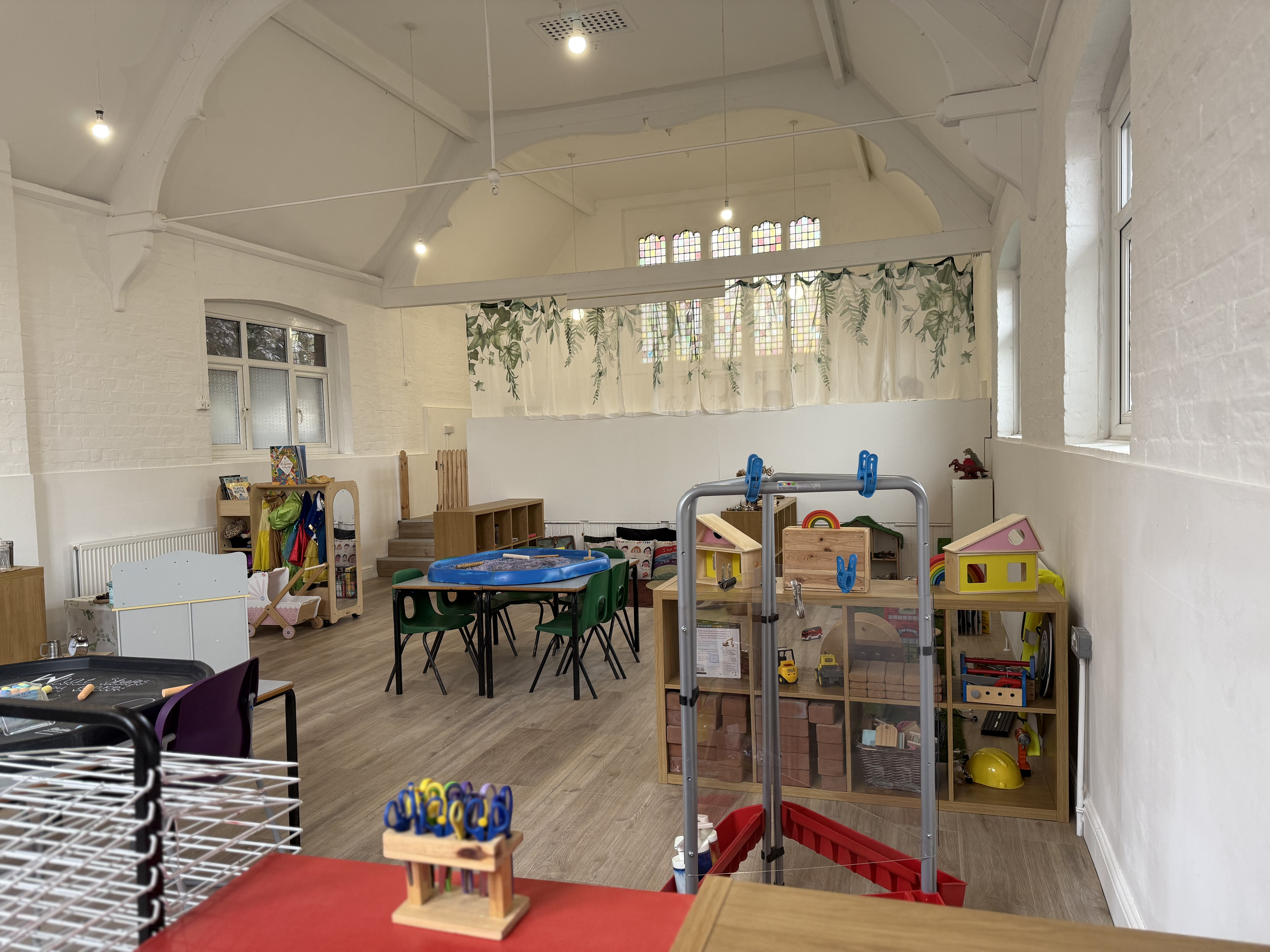 A children's playroom with white brick walls, wooden flooring, and large windows at Pop-Up Day Nursery