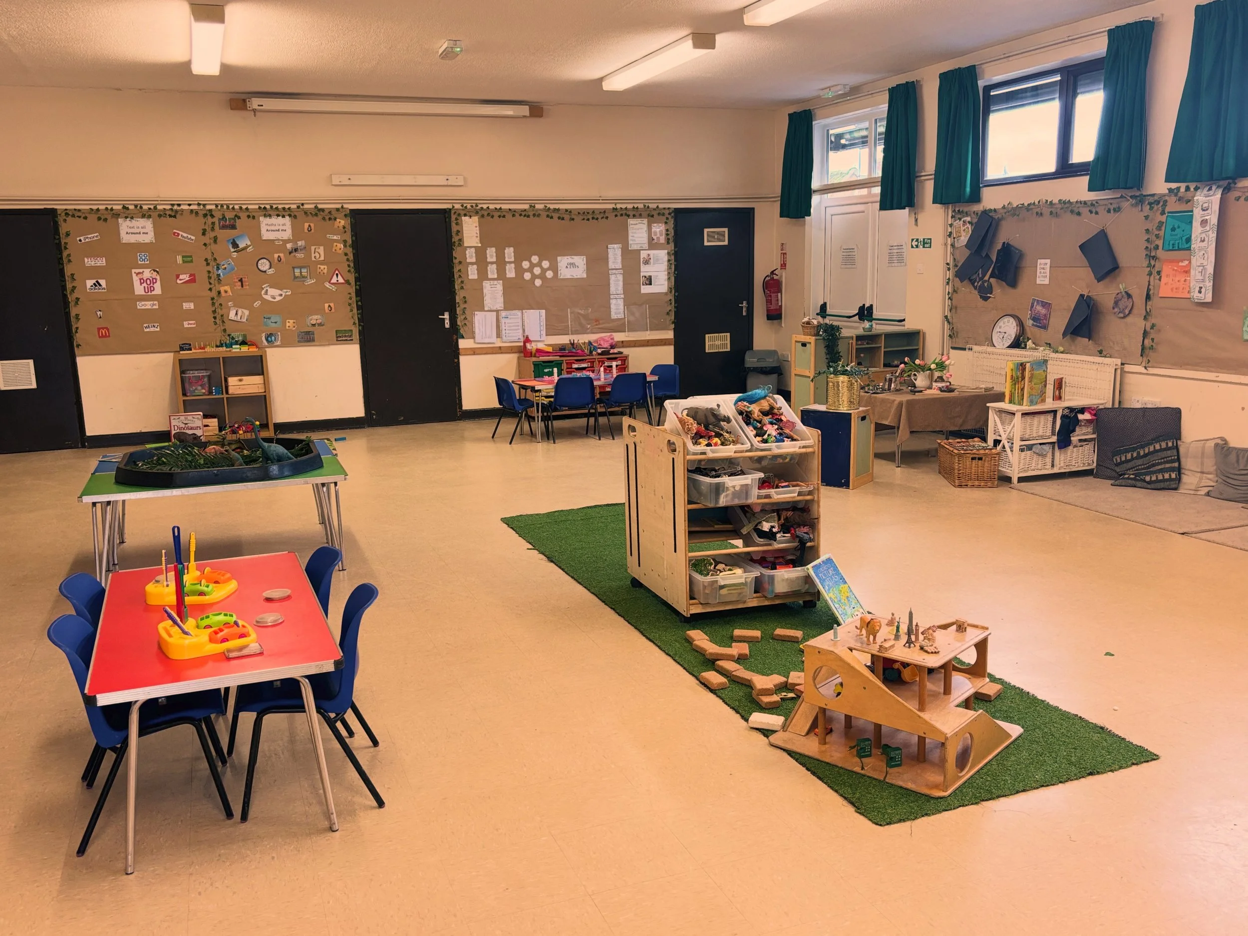Empty classroom with tables and chairs, toy display, educational materials, and posters on the walls at Pop-Up day Nursery
