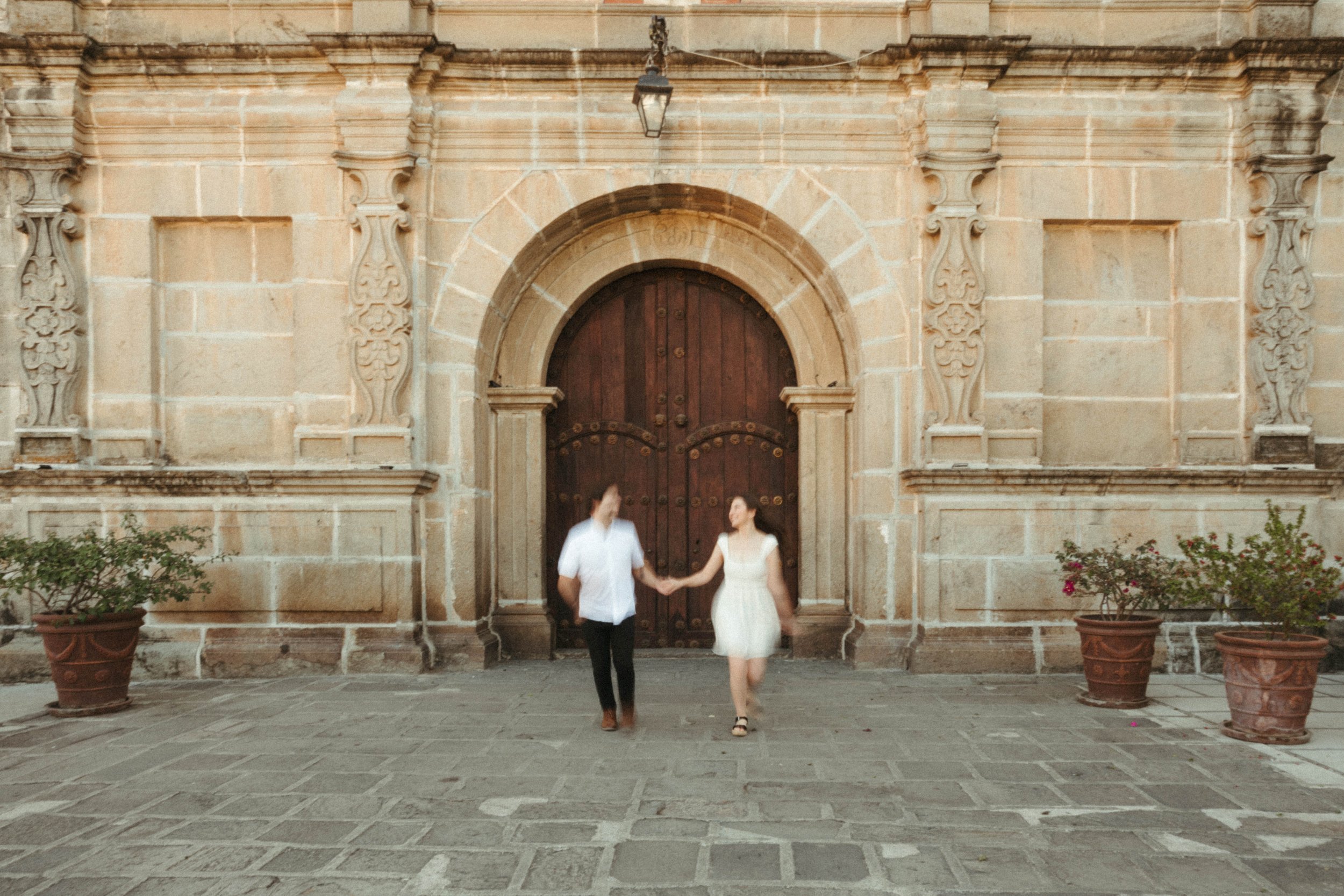 Couple running in front of one of the many churches in the cobblestone city of Antigua Guatemala, captured during an engagement photography session.