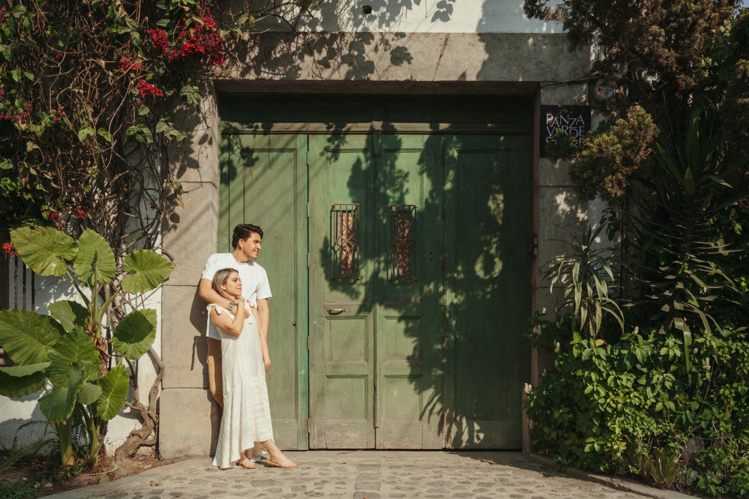 Couple standing in front of a green colonial door in Antigua Guatemala during a romantic engagement photography session.
