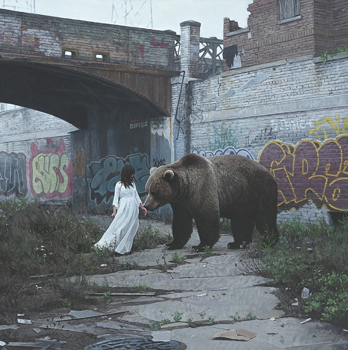 A person in a white dress holding hands with a bear in an urban alleyway surrounded by graffiti on the walls.