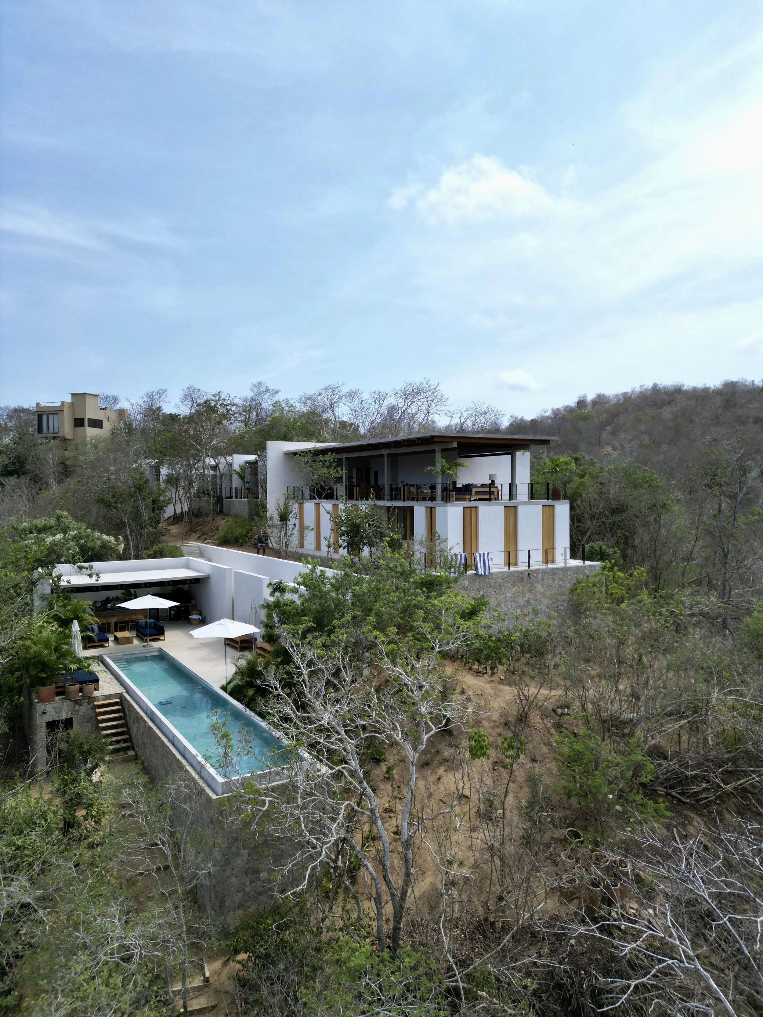 Drone photo of the final project. Left corner the pool area with the pool going further into the canopy of the trees. Shared space is an open space with a slick slab covering the kitchen area. on the centre it's the main house.