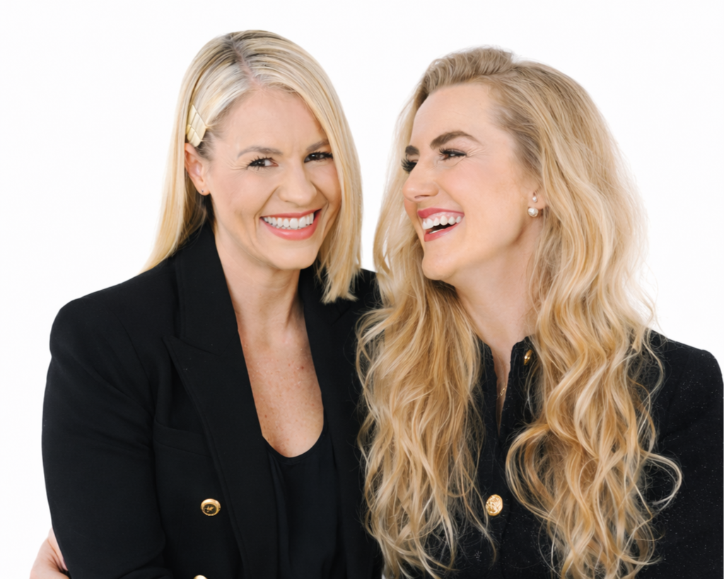 Zwei lachende Frauen mit blondem Haar, schwarz gekleidet, vor weißem Hintergrund.