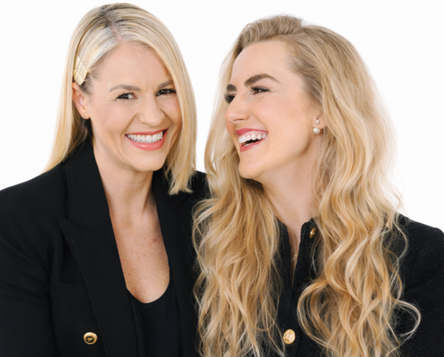 Zwei lachende Frauen tragen schwarze Kleidung, eines mit einem Latzknoten, die andere mit großen Ohrringen, vor weißem Hintergrund.