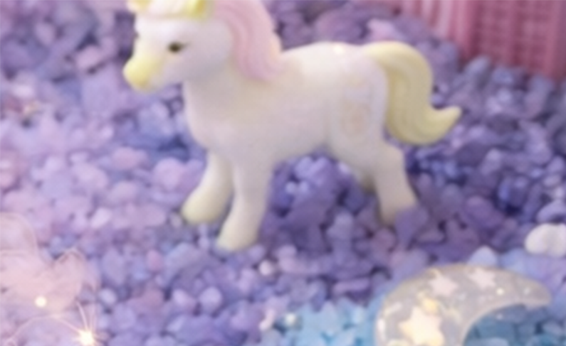 Weißer Plüsch-Pony mit gelber Mähne und Schweif auf einer blaulila gestreuten Unterlage.