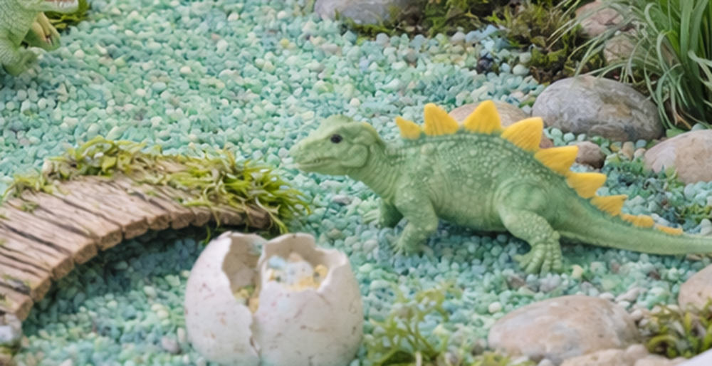 Ein Spielzeug-Krokodil in einem künstlichen Sandkasten mit Steinen und Pflanzen.