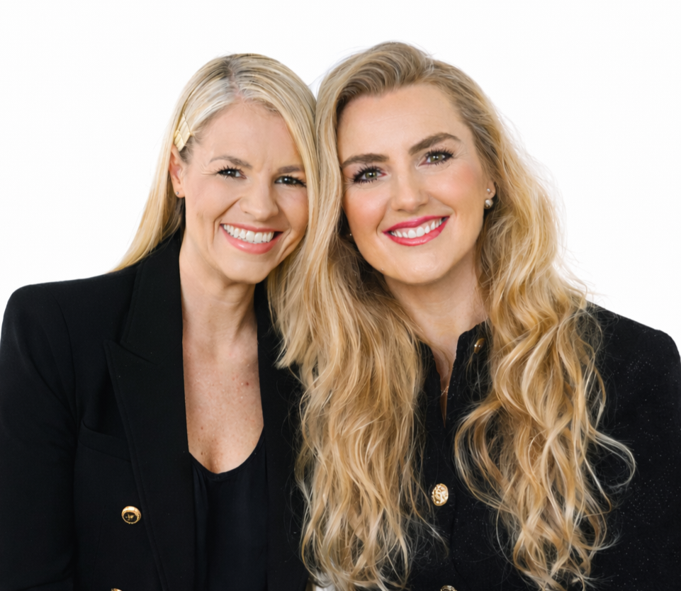 Zwei lachende Frauen mit langen Haaren, die schwarze Kleidung tragen, fotografiert gegen weißen Hintergrund.