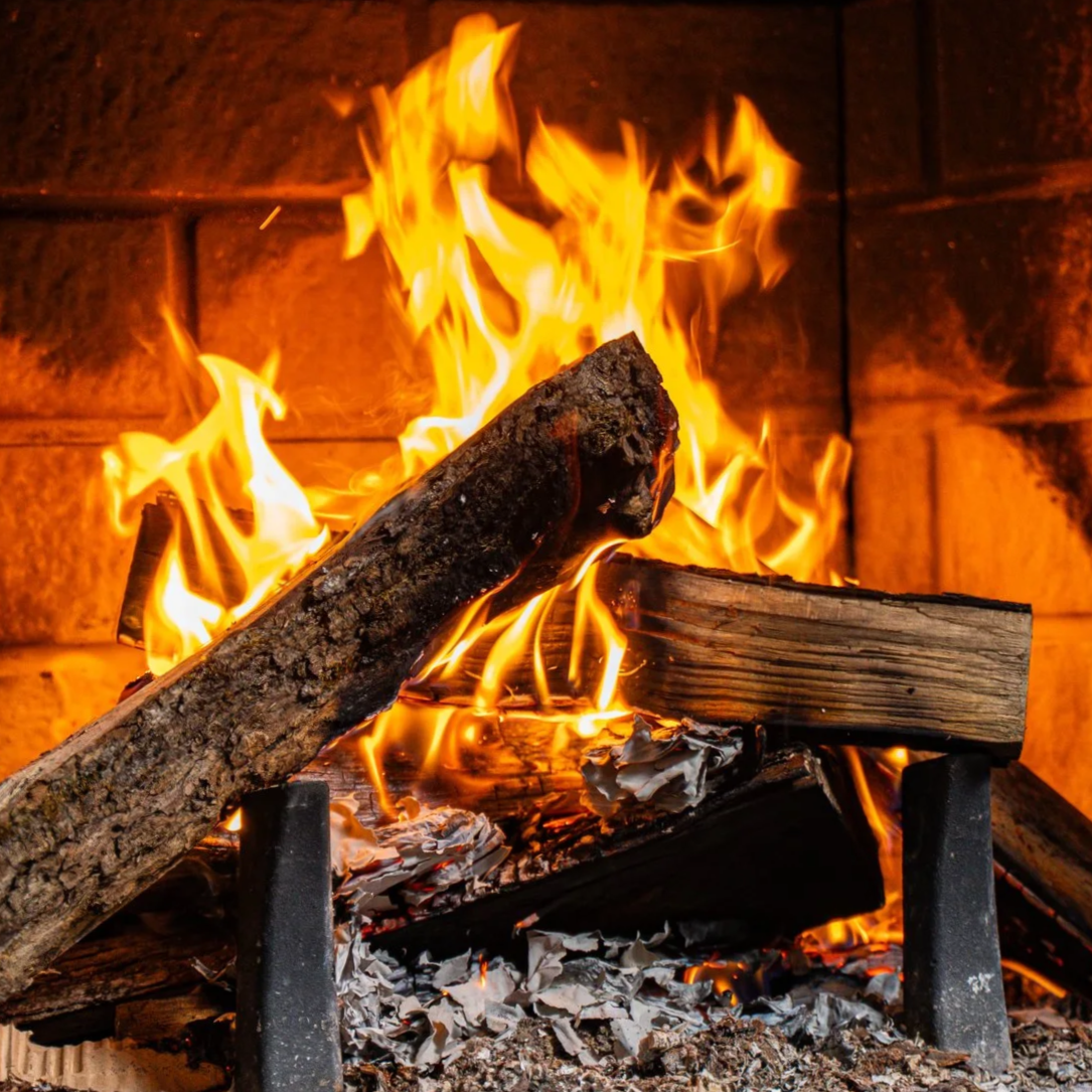 Un feu de cheminée avec des bûches en bois en train de brûler, avec des flammes orange et jaunes, et du papier recyclé brûlé en dessous.
