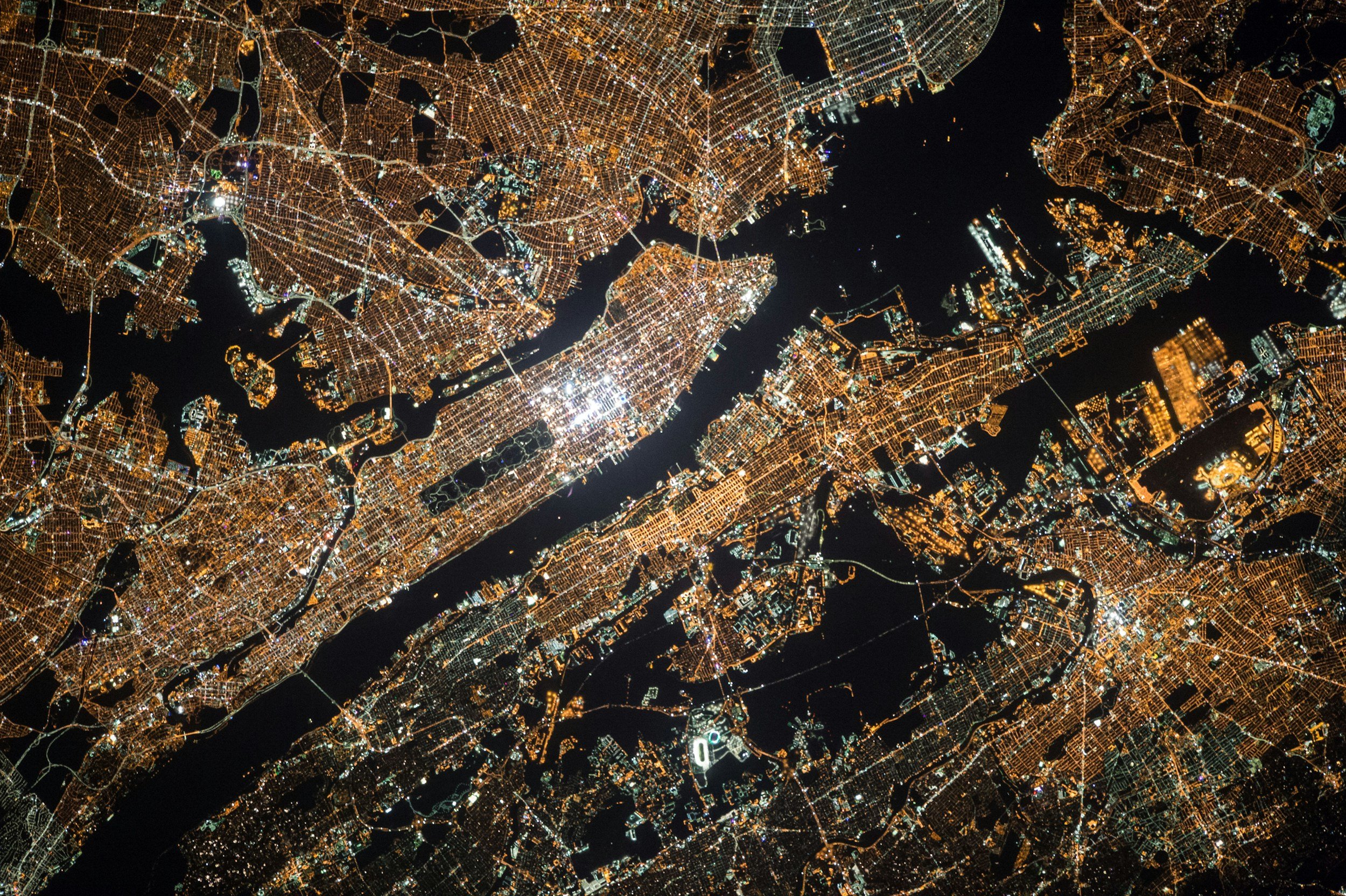 An aerial nighttime view of a city showing illuminated streets, bridges, and water bodies.